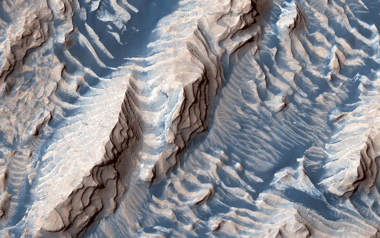 This image shows sedimentary rock and sand within Danielson Crater, an impact crater 67 kilometers in diameter, located in the southwest Arabia Terra region of Mars. The rock was formed millions or billions of years ago when loose sediments settled into the crater, one layer at a time, and were later cemented in place. Cyclical variations in the sediment properties made some layers more resistant to erosion than others. After eons, these tougher layers protrude outward like stair steps. Across these steps, the winds have scattered sand (typically appearing darker and less red, i.e. "bluer" in contrast-enhanced color), giving rise to the zebra stripe-like patterns visible here. This image completes a stereo pair over this location, which will allow measurement of the thicknesses of these sedimentary layers. The layer thicknesses and how they vary through time can provide some insight into the processes, possibly linked to ancient climate, that deposited the layers so long ago. https://photojournal.jpl.nasa.gov/catalog/PIA23454