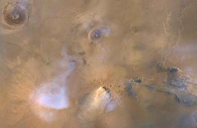 The yellow-white cloud in the bottom-center of this image is a Mars "dust tower" — a concentrated cloud of dust that can be lofted dozens of miles above the surface. The blue-white plumes are water vapor clouds. Olympus Mons, the tallest volcano in the solar system, is visible in the upper left corner, while Valles Marineris can be seen in the lower right.  Heat-sensitive instruments like the Mars Climate Sounder, carried aboard NASA's Mars Reconnaissance Orbiter (MRO), can map the formation of these dust towers, which form almost continuously during global dust storms.  Taken on Nov. 30, 2010, the image was produced by MRO's Mars Color Imager (MARCI), which was built and is operated by Malin Space Science Systems in San Diego.  https://photojournal.jpl.nasa.gov/catalog/PIA23513