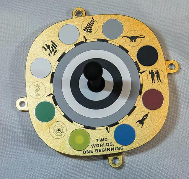 The primary calibration target for Mastcam-Z, a pair of zoomable cameras aboard NASA's Perseverance Mars rover, features color swatches used by scientists to fine-tune the cameras' settings. The object in the center, known as a shadow post, helps scientists check the color of the sky to calibrate for lighting conditions.  Symbols and mottos relevant to the mission are included around the target's perimeter: (clockwise from top) a fern; an Apatosaurus; a man and woman raising their hands in greeting (a nod to plaques carried aboard Pioneer 10 and 11, as well as the Golden Record aboard Voyagers 1 and 2); a rocket traveling from Earth (blue dot) to Mars (red dot); a motto reading "Two Worlds, One Beginning," in reference to the idea of Earth and the Red Planet growing out of the same proto-stellar dust; a model of the inner solar system; a DNA helix; and cyanobacteria, one of the earliest forms of life on Earth.  A key objective for Perseverance's mission on Mars is astrobiology, including the search for signs of ancient microbial life. The rover will characterize the planet's geology and past climate, pave the way for human exploration of the Red Planet, and be the first mission to collect and cache Martian rock and regolith (broken rock and dust).  https://photojournal.jpl.nasa.gov/catalog/PIA24178