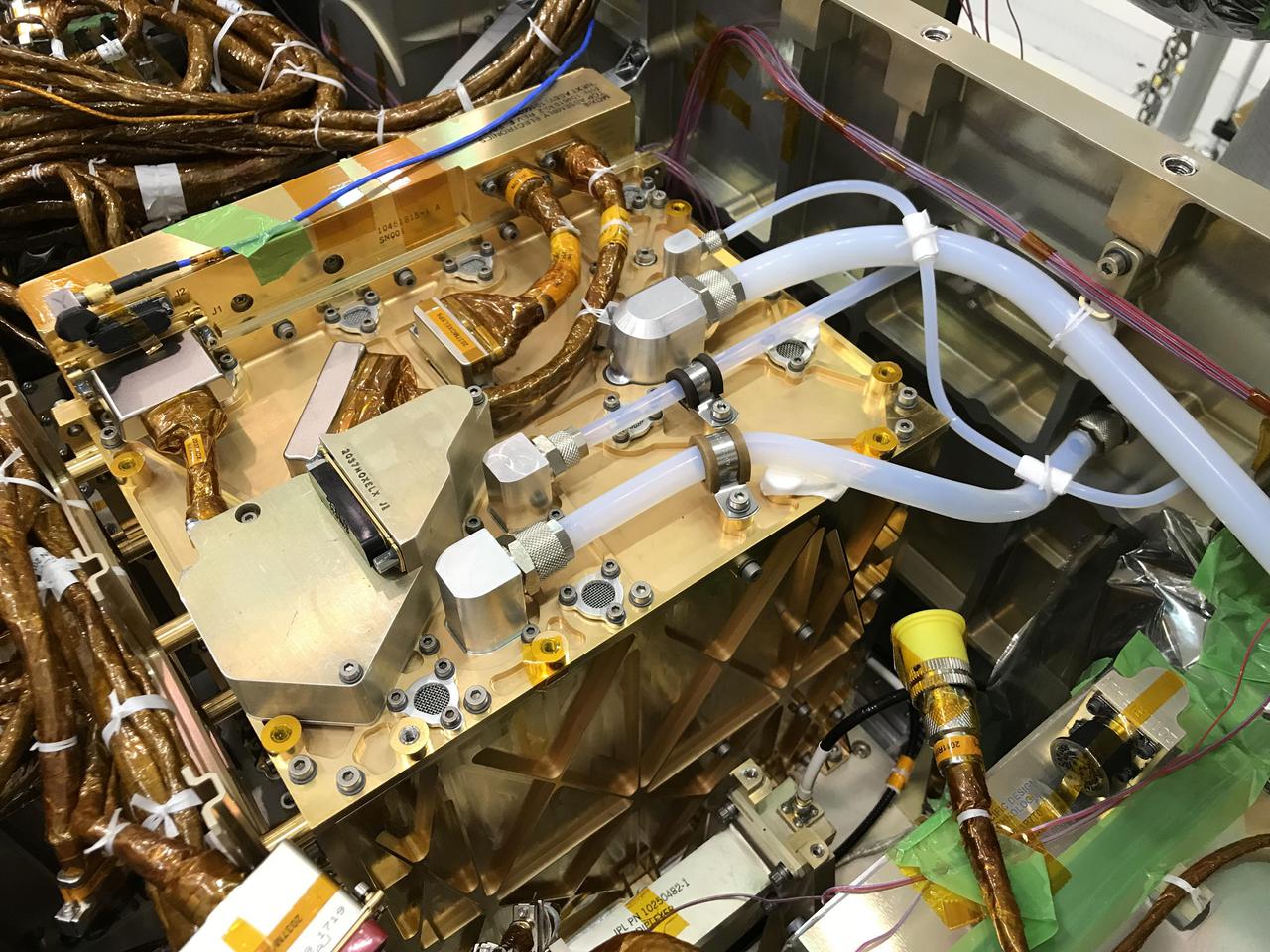In this image, the gold-plated Mars Oxygen In-Situ Resource Utilization Experiment (MOXIE) Instrument shines after being installed inside the Perseverance rover. The largest white tube on the top surface of MOXIE takes in filtered carbon dioxide-rich Martian atmosphere. That CO2 is pressurized and passed through the Solid Oxide Electrolysis unit, where it is split into carbon monoxide and oxygen. The smallest tube snaking across the top of the unit sends the oxygen produced by MOXIE through a composition sensor to measure purity, then vents the oxygen out to the Martian atmosphere. This technology demonstration may guide the design of future, larger devices that could enable human exploration of Mars.  https://photojournal.jpl.nasa.gov/catalog/PIA24203