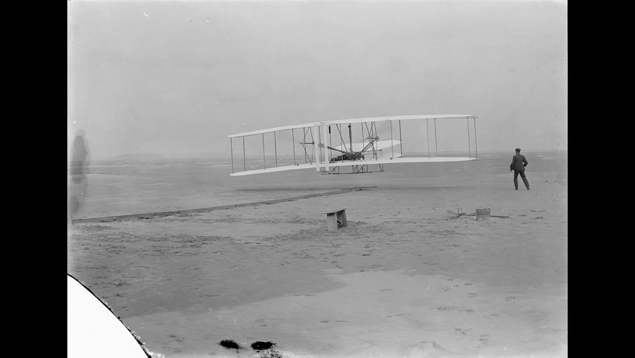 Orville Wright makes the first powered, controlled flight on Earth as his brother Wilbur looks on in this image taken at Kitty Hawk, North Carolina, on Dec. 17, 1903. Orville Wright covered 120 feet in 12 seconds during the first flight. The Wright brothers made four flights that day, each longer than the last.  A small amount of the material that covered the wing of the aircraft, Flyer 1, during the first flight was flown to Mars aboard NASA's Ingenuity Mars Helicopter. An insulative tape was used to wrap the small swatch of fabric around a cable located underneath the helicopter's solar panel. Ingenuity is scheduled to attempt the first powered, controlled flight on another planet in April 2021. The Wrights had been using the same type of material – an unbleached muslin called "Pride of the West" – to cover their glider and aircraft wings since 1901. A different piece of the material, along with a small splinter of wood, from the Flyer 1 was flown to the Moon and back aboard Apollo 11.  The image was taken by John Daniels, a member of the U.S. Life-Saving Station in Kill Devil Hills, North Carolina. Until the day of the flight, Daniels had never seen a camera.  https://photojournal.jpl.nasa.gov/catalog/PIA24434