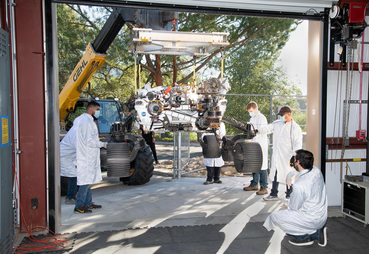 On Oct. 29, 2021, a heavy-duty vehicle transports the Perseverance rover's engineering model from a test lab to the Mars Yard garage at NASA's Jet Propulsion Laboratory. Short for Operational Perseverance Twin for Integration of Mechanisms and Instruments Sent to Mars, OPTIMISM is generically referred to as a vehicle system test bed.  As with vehicle system test beds for other Mars rovers, OPTIMISM is used to test moves and scenarios in the Mars Yard's simulated Red Planet landscape to help ensure that its twin on Mars can safely execute the commands sent by Earth-bound controllers. The tests could also potentially reveal unexpected problems Perseverance might encounter. With longer drives in Perseverance's near future, another job for OPTIMISM will involve presenting new challenges to the rover's autonomous navigation system, or AutoNav.  A key objective for Perseverance's mission on Mars is astrobiology, including the search for signs of ancient microbial life. The rover will characterize the planet's geology and past climate, pave the way for human exploration of the Red Planet, and be the first mission to collect and cache Martian rock and regolith (broken rock and dust).  Subsequent NASA missions, in cooperation with ESA (European Space Agency), would send spacecraft to Mars to collect these sealed samples from the surface and return them to Earth for in-depth analysis.  The Mars 2020 Perseverance mission is part of NASA's Moon to Mars exploration approach, which includes Artemis missions to the Moon that will help prepare for human exploration of the Red Planet.  https://photojournal.jpl.nasa.gov/catalog/PIA24526