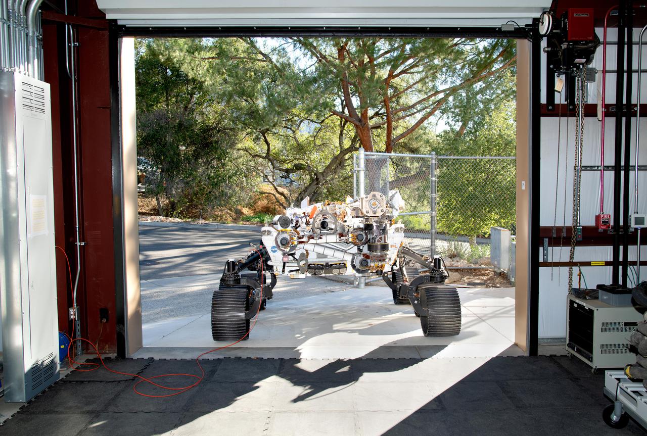 Short for Operational Perseverance Twin for Integration of Mechanisms and Instruments Sent to Mars, OPTIMISM faces a doorway of the Mars Yard garage at NASA's Jet Propulsion Laboratory on Oct. 29, 2021. Referred to generically as a vehicle system test bed, OPTIMISM was recently updated with additional mobility software and the bulk of the complex sample caching system.  As with vehicle system test beds for other Mars rovers, OPTIMISM is used to test moves and scenarios in the Mars Yard's simulated Red Planet landscape to help ensure that its twin on Mars can safely execute the commands sent by Earth-bound controllers. The tests could also potentially reveal unexpected problems Perseverance might encounter. With longer drives in Perseverance's near future, another job for OPTIMISM will involve presenting new challenges to the rover's autonomous navigation system, or AutoNav.  A key objective for Perseverance's mission on Mars is astrobiology, including the search for signs of ancient microbial life. The rover will characterize the planet's geology and past climate, pave the way for human exploration of the Red Planet, and be the first mission to collect and cache Martian rock and regolith (broken rock and dust).  Subsequent NASA missions, in cooperation with ESA (European Space Agency), would send spacecraft to Mars to collect these sealed samples from the surface and return them to Earth for in-depth analysis.  The Mars 2020 Perseverance mission is part of NASA's Moon to Mars exploration approach, which includes Artemis missions to the Moon that will help prepare for human exploration of the Red Planet.  https://photojournal.jpl.nasa.gov/catalog/PIA24527