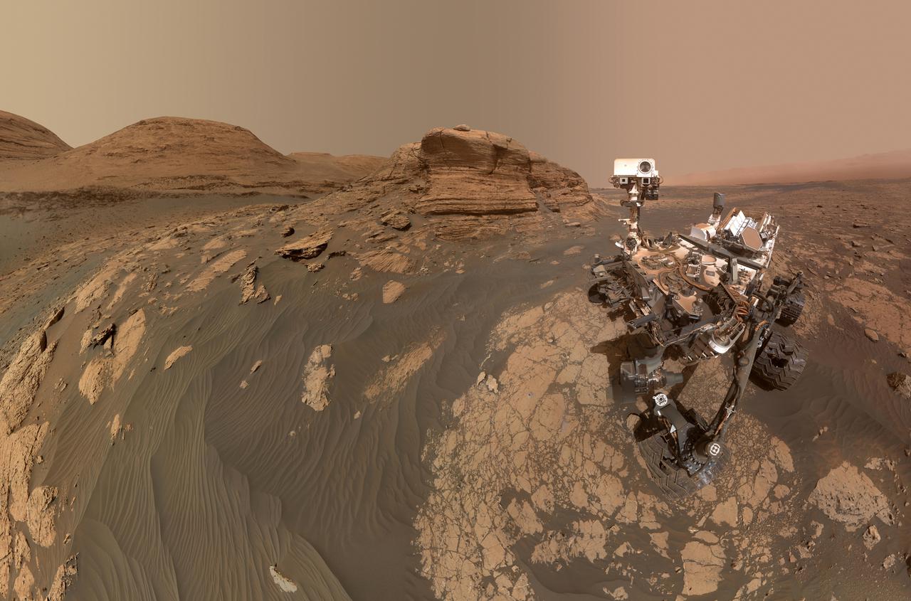 NASA's Curiosity Mars rover used two different cameras to create this selfie in front of Mont Mercou, a rock outcrop that stands 20 feet (6 meters) tall. The panorama is made up of 60 images taken by the Mars Hand Lens Imager (MAHLI) on the rover's robotic arm on March 26, 2021, the 3070th Martian day, or sol, of the mission. These were combined with 11 images taken by the Mastcam on the mast, or "head," of the rover on March 16, 2021, the 3,060th Martian day of the mission.  The hole visible to the left of the rover is where its robotic drill sampled a rock nicknamed "Nontron." The Curiosity team is nicknaming features in this part of Mars using names from the region around the village of Nontron in southwestern France.  https://photojournal.jpl.nasa.gov/catalog/PIA24543