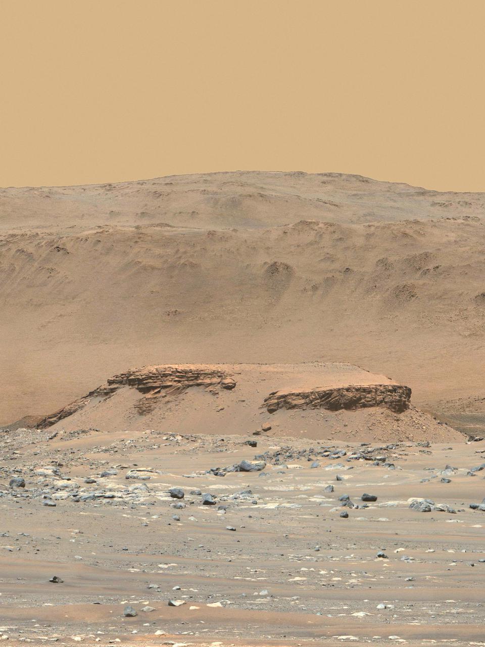 This enhanced-color image of Mars' Jezero Crater was taken by the Mastcam-Z instrument aboard NASA's Perseverance rover on April 18, 2021. The foreground flat-topped hill, informally named "Kodiak," is 1.4 miles (2.2 kilometers) from the rover and 820 feet (250 meters) wide. It exposes ancient layered rocks that indicate gradual deposition of sediments in a river delta, followed by floods.  The color bands of the image have been processed to improve visual contrast and accentuate color differences.  The Mastcam-Z investigation is led and operated by Arizona State University in Tempe, working in collaboration with Malin Space Science Systems in San Diego, California, on the design, fabrication, testing, and operation of the cameras, and in collaboration with the Neils Bohr Institute of the University of Copenhagen on the design, fabrication, and testing of the calibration targets.  A key objective for Perseverance's mission on Mars is astrobiology, including the search for signs of ancient microbial life. The rover will characterize the planet's geology and past climate, pave the way for human exploration of the Red Planet, and be the first mission to collect and cache Martian rock and regolith (broken rock and dust).  Subsequent NASA missions, in cooperation with ESA (European Space Agency), would send spacecraft to Mars to collect these sealed samples from the surface and return them to Earth for in-depth analysis.  The Mars 2020 Perseverance mission is part of NASA's Moon to Mars exploration approach, which includes Artemis missions to the Moon that will help prepare for human exploration of the Red Planet.  https://photojournal.jpl.nasa.gov/catalog/PIA24802