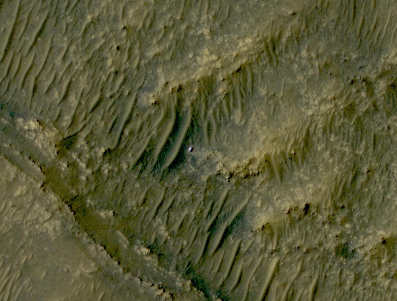 The white speck is NASA's Perseverance rover in the "South Séítah" area of Mars' Jezero Crater. The image was taken by the agency's Mars Reconnaissance Orbiter using its High-Resolution Imaging Science Experiment, or HiRISE, camera.  The University of Arizona, in Tucson, operates HiRISE, which was built by Ball Aerospace & Technologies Corp., in Boulder, Colorado. NASA's Jet Propulsion Laboratory, a division of Caltech in Pasadena, California, manages the Mars Reconnaissance Orbiter Project for NASA's Science Mission Directorate in Washington.  A key objective for Perseverance's mission on Mars is astrobiology, including the search for signs of ancient microbial life. The rover will characterize the planet's geology and past climate, pave the way for human exploration of the Red Planet, and be the first mission to collect and cache Martian rock and regolith (broken rock and dust).  Subsequent NASA missions, in cooperation with ESA (European Space Agency), would send spacecraft to Mars to collect these sealed samples from the surface and return them to Earth for in-depth analysis.  The Mars 2020 Perseverance mission is part of NASA's Moon to Mars exploration approach, which includes Artemis missions to the Moon that will help prepare for human exploration of the Red Planet.  https://photojournal.jpl.nasa.gov/catalog/PIA24837