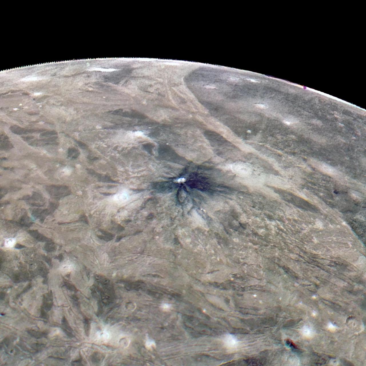 This look at the complex surface of Jupiter's moon Ganymede came from NASA's Juno mission during a close pass by the giant moon in June 2021. At closest approach, the spacecraft came within just 650 miles (1,046 kilometers) of Ganymede's surface.  Most of Ganymede's craters have bright rays extending from the impact scar, but about 1 percent of the craters have dark rays. This image taken by JunoCam during the close Ganymede pass shows one of the dark-rayed craters. The crater, named Kittu, is about 9 miles (15 kilometers) across, surrounded by darker material ejected during the impact that formed the crater. Scientists believe that contamination from the impactor produced the dark rays. As time passes, the rays stay dark because they are a bit warmer than the surroundings, so ice is driven off to condense on nearby colder, brighter terrain.  Ganymede is the largest moon in our solar system, larger even than the planet Mercury. It's the only moon known to have its own magnetic field, which causes auroras that circle the moon's poles. Evidence also indicates Ganymede may hide a liquid water ocean beneath its icy surface.  Citizen scientist Thomas Thomopoulos created this enhanced-color image using data from the JunoCam camera. The original image was taken on June 7, 2021.  https://photojournal.jpl.nasa.gov/catalog/PIA25012