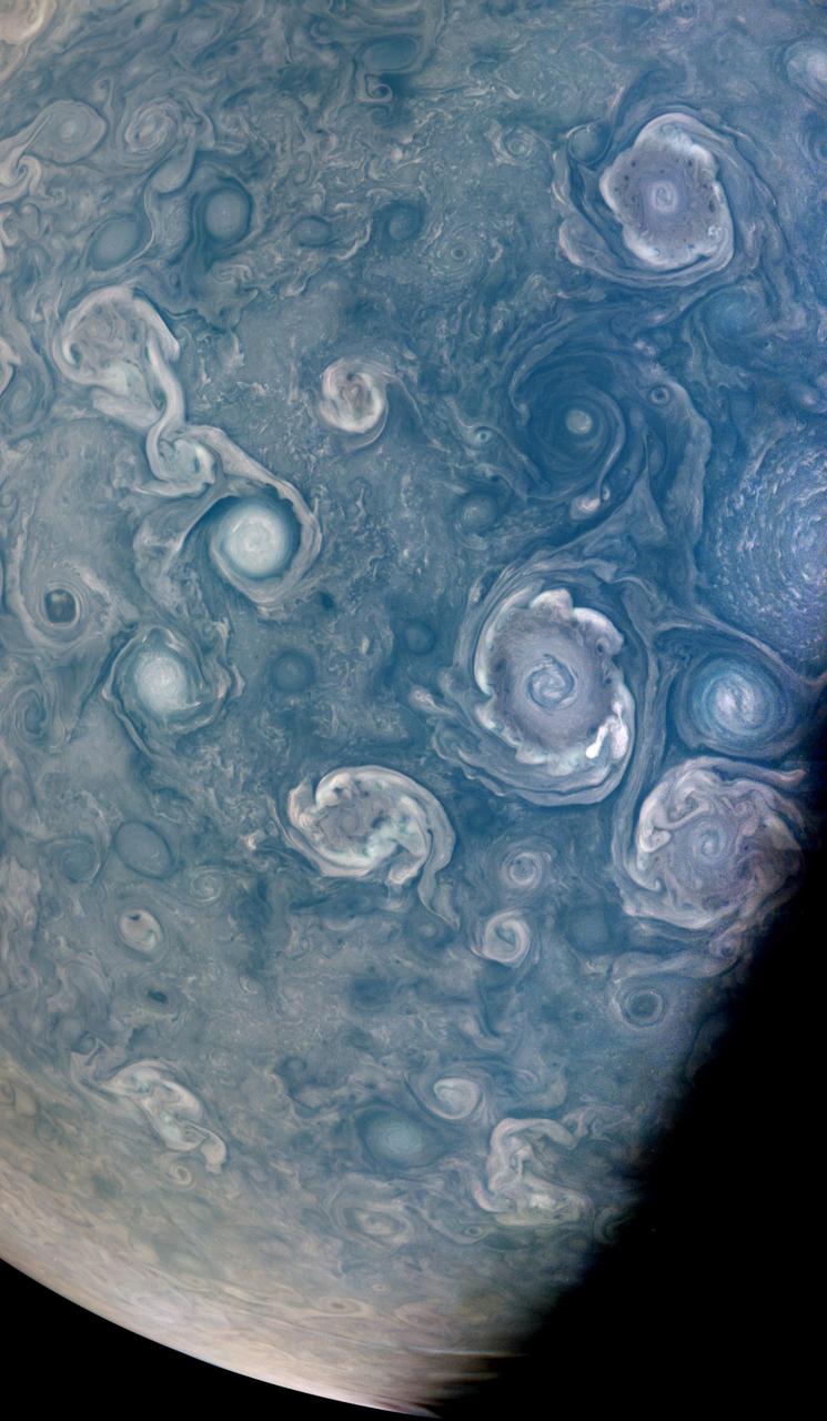 As NASA's Juno mission completed its 43rd close flyby of Jupiter on July 5, 2022, its JunoCam instrument captured this striking view of vortices – hurricane-like spiral wind patterns – near the planet's north pole.  These powerful storms can be over 30 miles (50 kilometers) in height and hundreds of miles across. Figuring out how they form is key to understanding Jupiter's atmosphere, as well as the fluid dynamics and cloud chemistry that create the planet's other atmospheric features. Scientists are particularly interested in the vortices' varying shapes, sizes, and colors. For example, cyclones, which spin counter-clockwise in the northern hemisphere and clockwise in the southern, and anti-cyclones, which rotate clockwise in the northern hemisphere and counter-clockwise in the southern hemisphere, exhibit very different colors and shapes.  A NASA citizen science project, Jovian Vortex Hunter, seeks help from volunteer members of the public to spot and help categorize vortices and other atmospheric phenomena visible in JunoCam photos of Jupiter. This process does not require specialized training or software, and can be done by anyone, anywhere, with a cellphone or laptop. As of July 2022, 2,404 volunteers had made 376,725 classifications using the Jovian Vortex Hunter project web site at https://www.zooniverse.org/projects/ramanakumars/jovian-vortex-hunter.  Another citizen scientist, Brian Swift, created this enhanced color and contrast view of vortices using raw JunoCam image data. At the time the raw image was taken, the Juno spacecraft was about 15,600 miles (25,100 kilometers) above Jupiter's cloud tops, at a latitude of about 84 degrees.  https://photojournal.jpl.nasa.gov/catalog/PIA25017