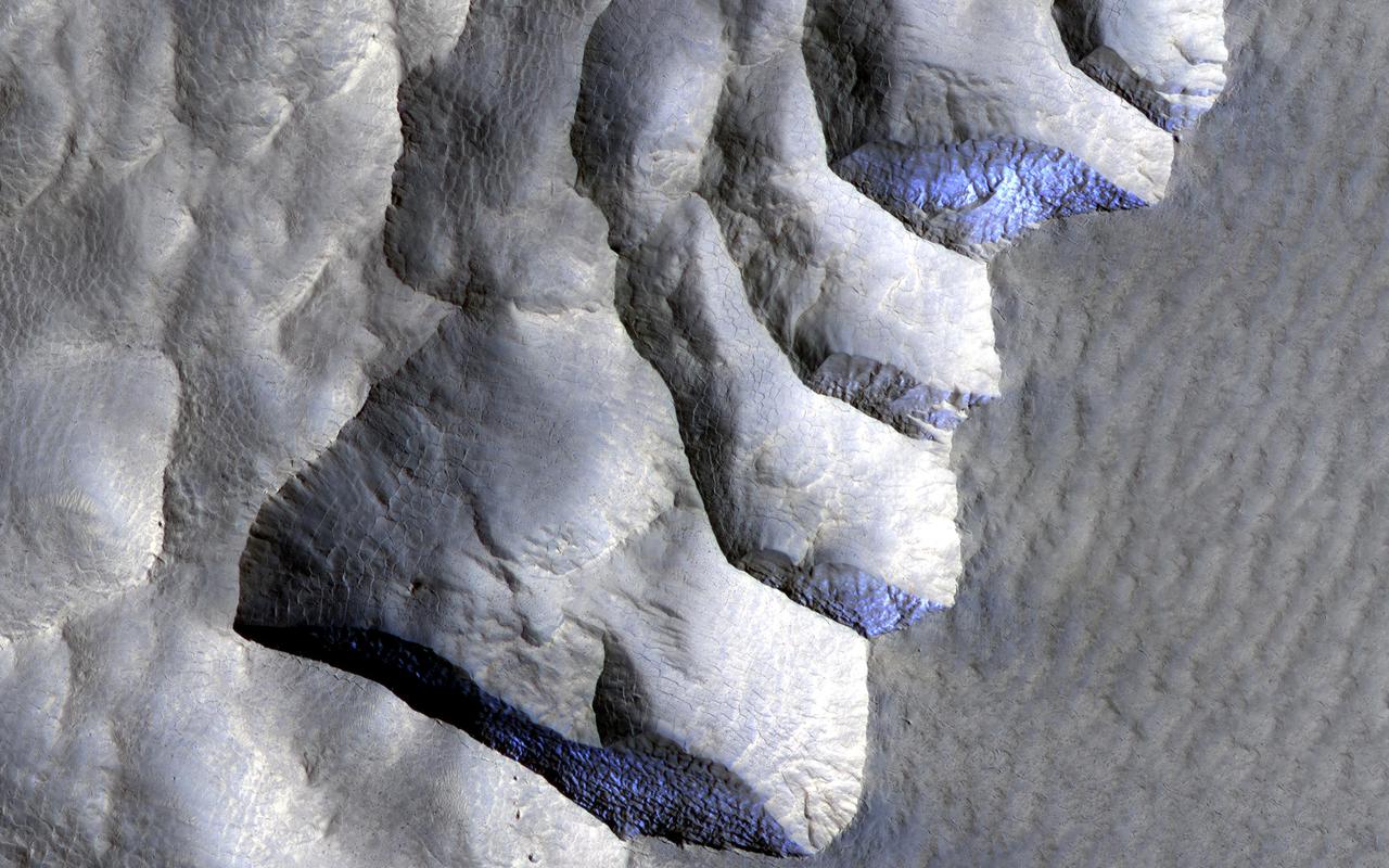 This area, on the western edge of Milankovic Crater on Mars, has a thick deposit of sediment that covers a layer rich in ice. The ice is not obvious unless you look in color. In the red-green-blue images that are close to what the human eye would see, the ice looks bright white, while the surroundings are a rusty red. The ice stands out even more clearly in the infrared-red-blue images where it has a striking bluish-purple tone while the surroundings have a yellowish-grey color. The ice-rich material is most visible when the cliff is oriented east-west and is shielded from the sun as it arcs through the sky to the south. https://photojournal.jpl.nasa.gov/catalog/PIA25088