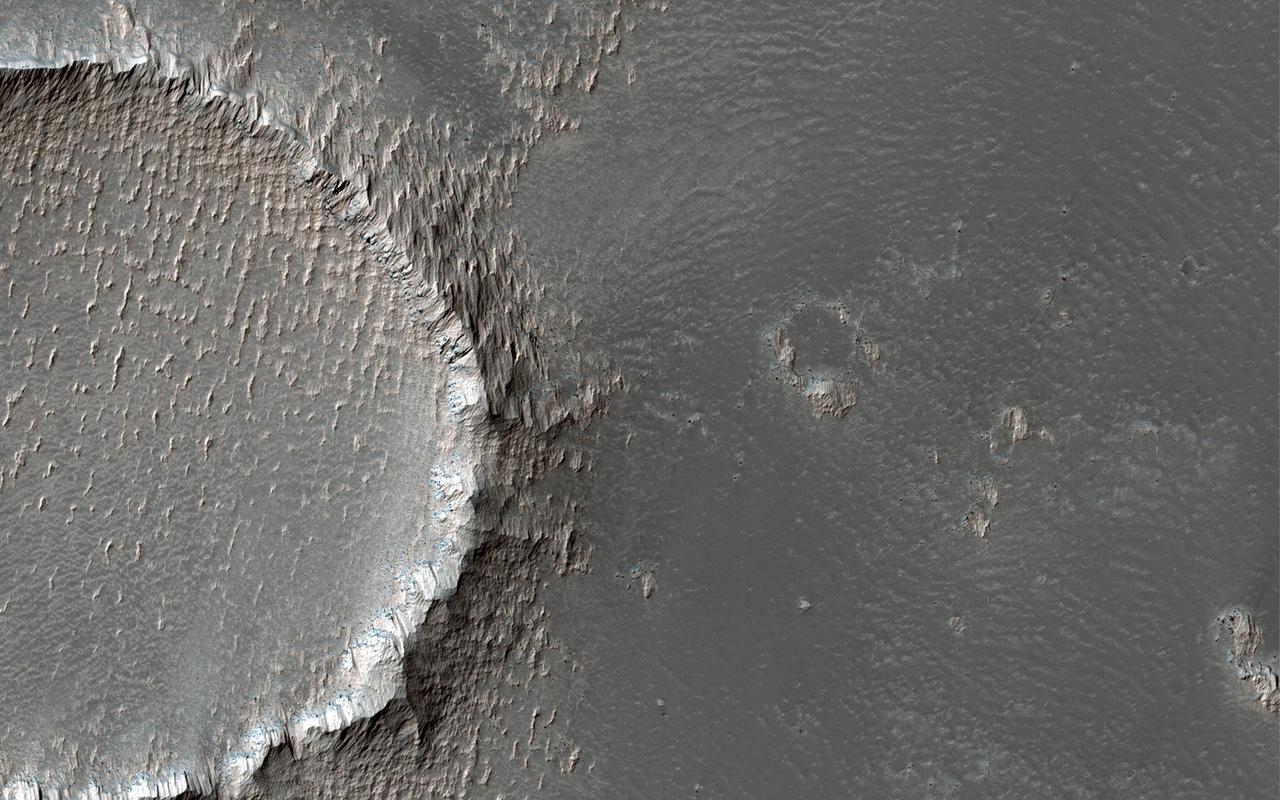 This image is located on the southeastern flank of a volcano on Mars called Arsia Mons. On the eastern side of the image, the lobate margin of an old lava flow is visible among brighter tones.  The upstanding rims of several degraded impact craters are also visible. In the detailed cutout, we can see that the bright tones are erosion resistant outcrops, likely from dust that has accumulated and been sculpted by the wind. (The small crater on the left of the cutout is 70 meters across.)  Arsia Mons is a shield volcano with a relatively low slope and a massive caldera at its summit.  https://photojournal.jpl.nasa.gov/catalog/PIA25184