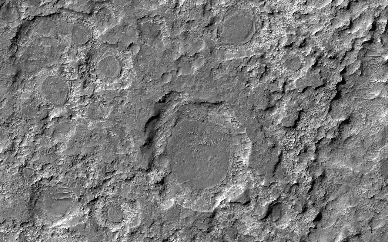 n the ancient past, this area of Mars was bombarded by impactors, forming craters of various sizes in the light-toned material. Some time after that, a darker material blanketed and covered the field, filling in the craters. Eventually, that blanketed material itself became rock. Long after that, erosive forces (likely wind) acted in this area removing both dark and light-toned material, like an archeologist using a brush to reveal buried structures. What we see today are a variety of dark circular features that are the remains of the layer that has been eroded back from the walls of the craters that formed them. In some cases, the crater rim is eroded and just a circular dark patch stands on a brighter exposure of rock. Studying the thickness and characteristics of the dark layer might help scientists learn more about the processes that deposited the material, as well as those that eroded it. https://photojournal.jpl.nasa.gov/catalog/PIA25187