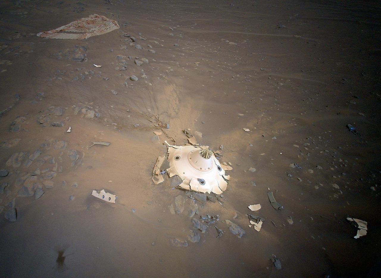 This image of Perseverance's backshell sitting upright on the surface of Jezero Crater was collected from an altitude of 26 feet (8 meters) by NASA's Ingenuity Mars Helicopter during its 26th flight at Mars on April 19, 2022. Engineers working on the Mars Sample Return program requested images be taken from an aerial perspective of the components because they may provide insight into the components' performance during the rover's entry, descent, and landing on Feb. 18, 2021.  The tangle of cables seen streaming out from the top of the backshell, and coated with Martian dust on the surface, are high-strength suspension lines that connect the backshell to Perseverance's supersonic parachute (upper left). The backshell and parachute helped protect the rover in deep space and during its fiery descent toward the Martian surface.  https://photojournal.jpl.nasa.gov/catalog/PIA25219
