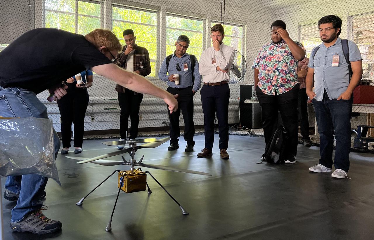 Participants in NASA's Minority Serving Institutions Space Accelerator program surround a full-scale model of NASA's Mars Ingenuity Helicopter as engineer Michael Starch discusses the mission. The group was visiting NASA's Jet Propulsion Laboratory on Aug. 18, 2022.      These participants were members of three teams named as awardees in the first-of-its-kind accelerator program, a competition to advance the NASA's goals and meet its needs in the areas of machine learning, artificial intelligence, and development of autonomous systems while also engaging underrepresented academic institutions and reducing barriers for them to submit ideas to the agency. The program provides funding, business training through a 10-week accelerator course, and mentorship to help the teams develop ideas for systems that can operate without human oversight for future science missions in space and on Earth.      The teams were made up of professors and students from Fayetteville State University in North Carolina, University of Massachusetts Boston, and California State University, Northridge. At the conclusion of the accelerator, participants arrived in Southern California for a variety of events, including two days at JPL.      The program is a partnership between NASA's Science Mission Directorate, its Earth Science Technology Office, the Minority University Research Education Project within the agency's Office of STEM Engagement, JPL, and Starburst, a global aerospace accelerator company based in Los Angeles.  https://photojournal.jpl.nasa.gov/catalog/PIA25315