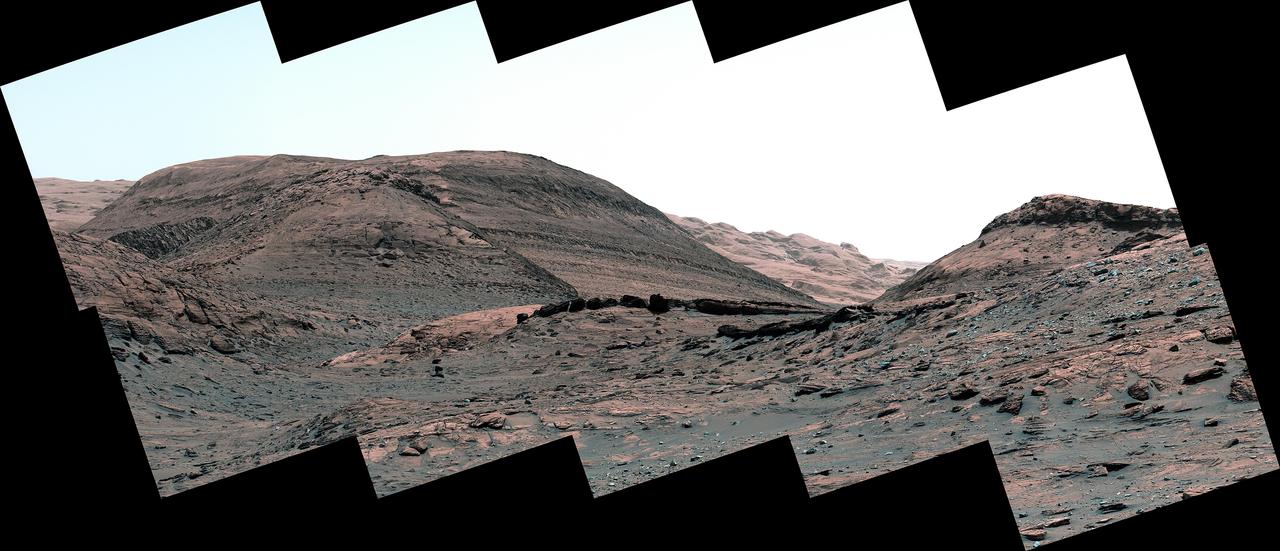 NASA's Curiosity Mars rover captured this view of a sulfate-bearing region ahead of its current location. Dark boulders near the center of the panorama are thought to have formed from sand deposited in ancient streams or ponds. Scattered gray rocks covering the hillside on the right are all that remain of a sandstone capping unit that once covered this area. This panorama is made up of 10 individual images that were captured by Curiosity's Mast Camera, or Mastcam, on May 2, 2022, the 3,462nd Martian day, or sol, of the mission. The images were stitched together after they were sent back to Earth. Behind the dark boulders – in the middle of the image – is a mountain that makes up part of the sulfate-bearing region; layers within this region can be seen as stripes across the mountainside. These layers represent an excellent record of how Mars' water and climate changed over time. https://photojournal.jpl.nasa.gov/catalog/PIA25367