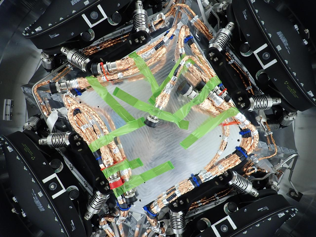 All four of the reaction wheels installed onto NASA's Europa Clipper are visible in this photo, which was shot from underneath the main body of the spacecraft while it is being assembled at the agency's Jet Propulsion Laboratory in Southern California.  The spacecraft is set to launch in October 2024 and will head toward Jupiter's moon Europa, where it will collect science observations while flying by the icy moon dozens of times. During its journey through deep space and its flybys of Europa, the spacecraft's reaction wheels rotate the orbiter so its antennas can communicate with Earth and so its science instruments, including cameras, can stay oriented toward Europa. Two feet wide and made of steel, aluminum, and titanium, the wheels spin rapidly to create a force that causes the orbiter to rotate in the opposite direction. The wheels will run on electricity provided by the spacecraft's vast solar arrays. The green tape that is visible here keeps cables temporarily secured during the wheel installation.  Scientists believe Europa harbors a vast internal ocean that may have conditions suitable for supporting life. Europa Clipper's suite of science instruments gathers data on the moon's atmosphere, surface, and interior – information that will help scientists learn more about the ocean, the ice crust, and potential plumes that may be venting subsurface water into space.  https://photojournal.jpl.nasa.gov/catalog/PIA25495