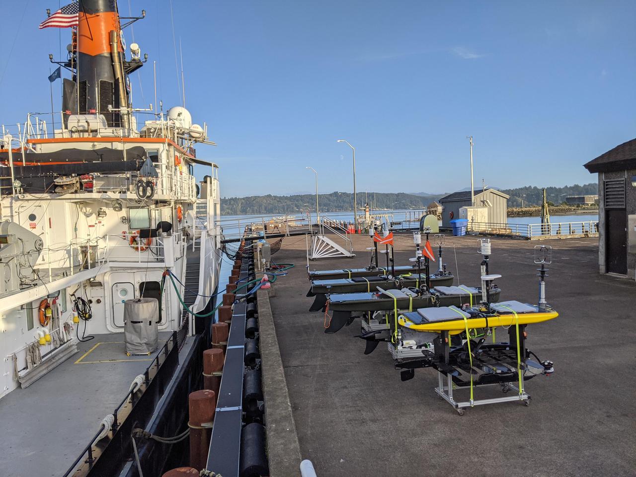 As part of NASA's Sub-Mesoscale Ocean Dynamics Experiment (S-MODE) pilot campaign in 2021, the research vessel Oceanus, owned by the National Science Foundation, set sail to an area 110 nautical miles off the coast of San Francisco, accompanied by a fleet of several types of autonomous marine research vessels.      The wave gliders pictured here on the dock carry a variety of sensors and instruments. Because they're autonomous, their use reduces the risk posed to human researchers who could be exposed to large storms at sea.      S-MODE is a NASA Earth mission to use newly developed in-situ and remote-sensing techniques to look at small-scale ocean whirlpools, eddies, and currents. The observations could help scientists better understand how these dynamics drive the give-and-take of material and energy between the ocean and atmosphere and, ultimately, help shape Earth's climate.      More information about S-MODE is at https://espo.nasa.gov/s-mode/content/S-MODE  https://photojournal.jpl.nasa.gov/catalog/PIA25524