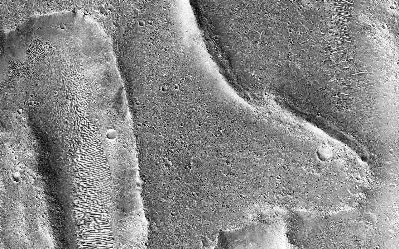 Ares Vallis is a large valley that was carved billions of years ago by water flowing across the surface of Mars. This image shows an area where the flowing water may have stripped away some of the rocks and soils at the bottom of the valley, leaving behind the ridge-like formations. In other areas of our observation, such as the smooth terrain in the middle portion of this image, the flowing water appears to have carried in and left behind rocks and soils from somewhere upstream. Scientists study landforms, rocks and soils such as these to understand how, where and when floods occurred in Mars' past. https://photojournal.jpl.nasa.gov/catalog/PIA25551