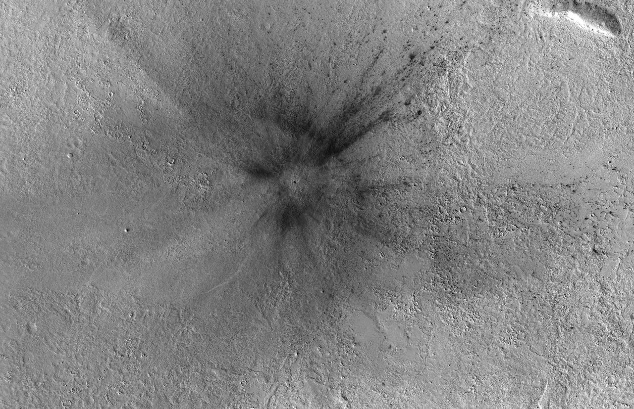 This meteoroid impact crater on Mars was discovered using the black-and-white Context Camera aboard NASA's Mars Reconnaissance Orbiter (MRO). The Context Camera took this image showing the impact, which occurred Dec. 24, 2021, in a region called Amazonis Planitia.  Relying on data from the Mars Color Imager camera, also aboard MRO, along with seismic data from NASA's InSight lander, scientists were able to determine when this particular crater formed.  Looking closely at the crater's rim, white specks could be detected that suggested the presence of water ice (which was later confirmed by MRO's High-Resolution Imaging Science Experiment, or HiRISE, camera). Debris thrown during the impact can be seen reaching as far as 23 miles (37 kilometers) away. The disturbance seen in the surface suggests the meteoroid was traveling towards the northeast when it hit the ground, throwing the longest streaks of debris in that direction.  https://photojournal.jpl.nasa.gov/catalog/PIA25584