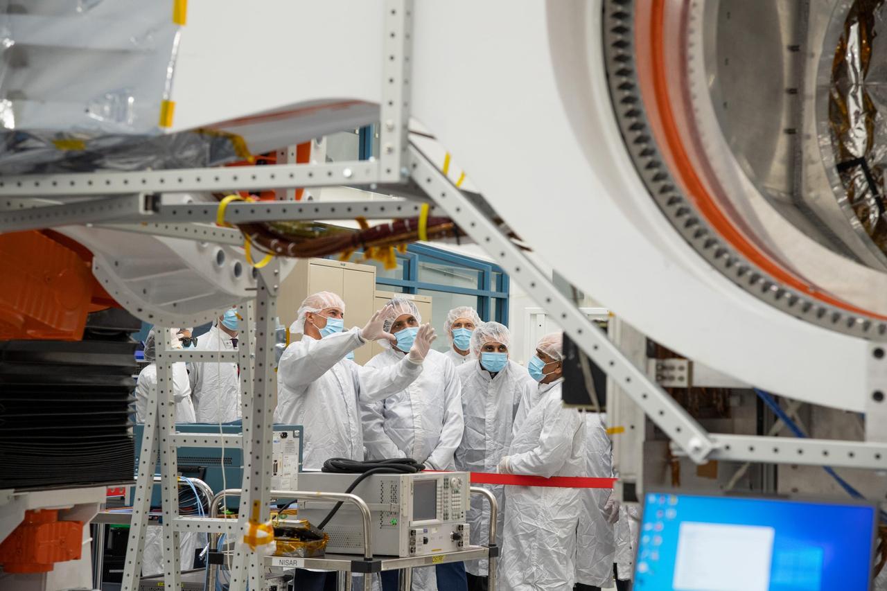 NASA's NISAR Project Manager Phil Barela (with hands raised) speaks with Indian Space Research Organisation Chairman S. Somanath about the NASA-ISRO Synthetic Aperture Radar (NISAR) science instrument payload in a clean room at NASA's Jet Propulsion Laboratory in Southern California on Feb. 3, 2023. Somanath was among a group of visitors to the facility that included officials from NASA, ISRO, and the Indian Embassy.      The NISAR mission – a joint effort between NASA and ISRO – will measure changes to Earth's land ice surfaces down to fractions of an inch. Data collected by this satellite will help researchers monitor a wide range of changes critical to life on Earth in unprecedented detail. This includes spotting warning signs of imminent volcanic eruptions, helping to monitor groundwater supplies, tracking the melt rate of ice sheets tied to sea level rise, and observing shifts in the distribution of vegetation around the world. The data will inform humanity's responses to urgent challenges posed by natural disasters and climate change, and help communities prepare for and manage hazards.      There are two instruments on the satellite that will send and receive radar signals to and from Earth's surface to make the mission's measurements. An L-band synthetic aperture radar (SAR), which uses a signal wavelength of around 9 inches (24 centimeters), and an S-band SAR with a signal wavelength of nearly 5 inches (12 centimeters). Both will bounce their microwave signal off of the planet's surface and record how long it takes the signal to make one roundtrip, as well as the strength of that return signal. This enables the researchers to calculate the distance from the spacecraft to Earth's surface and thereby determine how the land or ice is changing. An antenna reflector nearly 40 feet (12 meters) in diameter, supported by a deployable boom, will focus the microwave signals sent and received by the SARs.      JPL, which is managed for NASA by Caltech in Pasadena, leads the U.S. component of NISAR and is providing the mission's L-band SAR instrument. NASA is also providing the radar reflector antenna, the deployable boom, a high-rate communication subsystem for science data, GPS receivers, a solid-state recorder, and payload data subsystem. ISRO is providing the spacecraft bus, the S-band SAR, the launch vehicle, and associated launch services and satellite mission operations.  https://photojournal.jpl.nasa.gov/catalog/PIA25598
