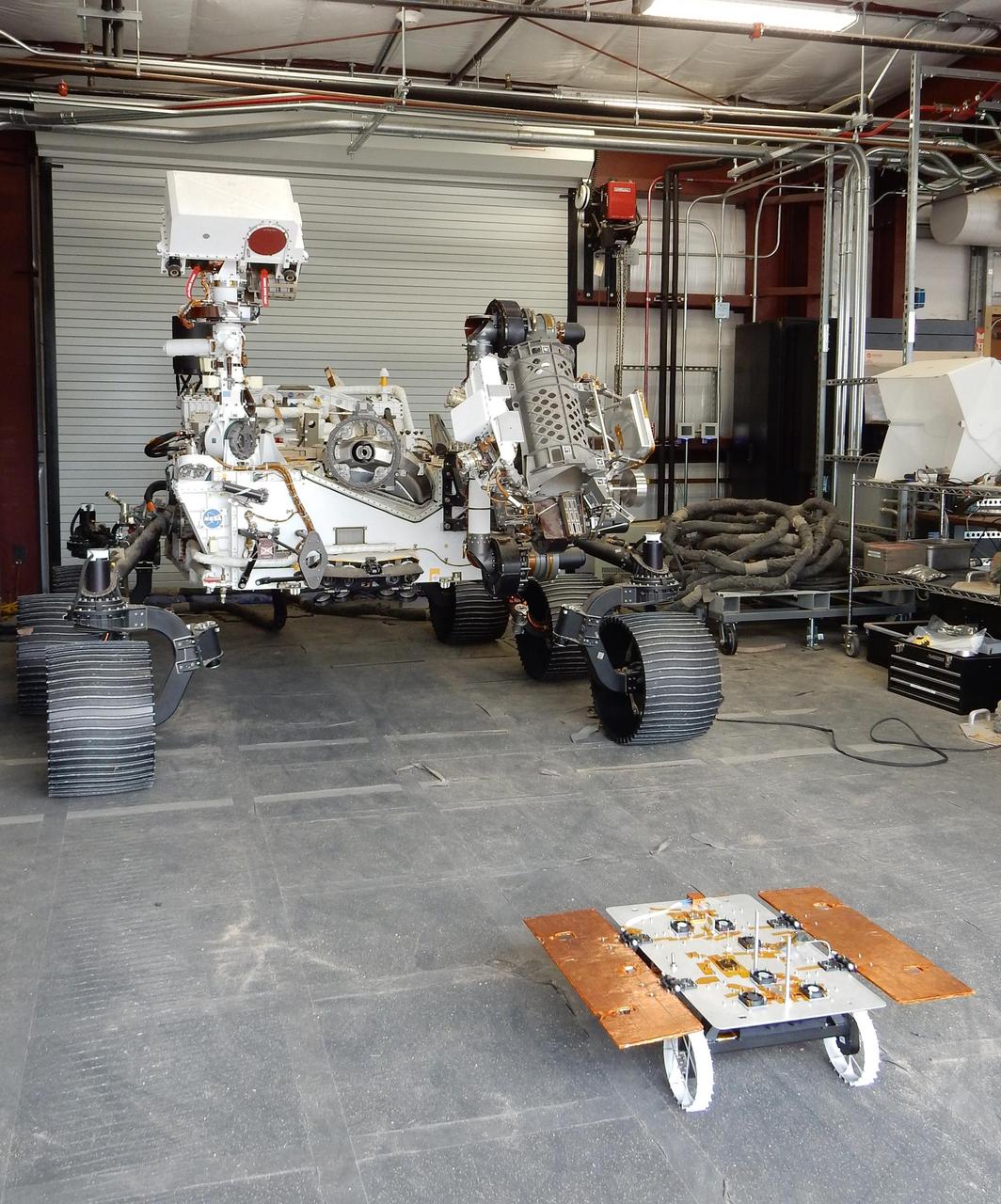 The Earth-bound full-scale engineering model of NASA's Perseverance rover, called OPTIMISM, seems to peer down at a much smaller CADRE rover in a building in the Mars Yard at NASA's Jet Propulsion Laboratory in Southern California in June 2023.  Short for Cooperative Autonomous Distributed Robotic Exploration, NASA's CADRE technology demonstration is slated to arrive at the Moon in spring 2024 as part of the agency's CLPS (Commercial Lunar Payload Services) initiative. CADRE is designed to demonstrate that multiple robots can cooperate and explore together autonomously – without direct input from human mission controllers.  The development rover being tested is similar in size and appearance to the flight models of the CADRE rovers, which are still being built.  A trio of the miniature solar-powered rovers, each about the size of a carry-on suitcase, will explore the Moon as a team, communicating via radio with each other and a base station aboard a lunar lander. By taking simultaneous measurements from multiple locations, CADRE will also demonstrate how multirobot missions can record data impossible for a single robot to achieve – a tantalizing prospect for future missions.  https://photojournal.jpl.nasa.gov/catalog/PIA25668