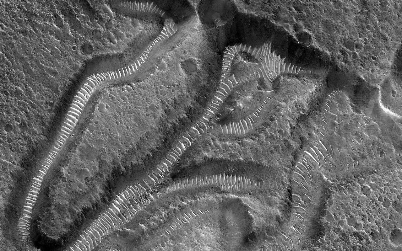 This image focuses on small channels formed on the floor of the much larger Kasei Valles, one of the largest outflow channels on Mars. The enormous floods that formed such channels sometimes flowed around either side of topographic rises forming islands with a streamlined shape. The channels in this image are located on the trailing edge of such a formation (white shaded box). The small channels formed linear coalescing pits, perhaps by ground ice sublimating into the atmosphere leaving the surface material to collapse. Much of the remaining material seems to be made up of easily eroded sediments likely deposited by the floodwaters, which have subsequently formed dunes inside the channels. Kasei extends almost 1600 kilometers (980 miles) across the surface towards the northeast before it empties into Chryse Planitia in the northern lowlands of Mars. https://photojournal.jpl.nasa.gov/catalog/PIA25702