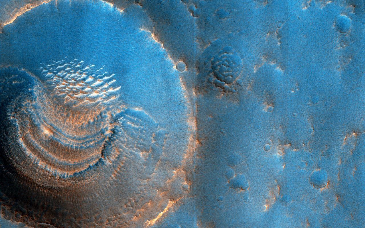 HiRISE images often raise more questions than answers. For example, this image of the northern plains of Arabia Terra shows craters that contain curious deposits with mysterious shapes and distribution.  The deposits are found only in craters larger than 600 meters in diameter and are absent from craters measuring 450 meters and less. The deposits are located on the south sides of the craters but not in the north (although the cutout shows a crater that also has windblown deposits in the north). The deposits have horizontal laminations that could be layers or terraces. The deposits also have radial striations formed by small bright ridges.  We suspect that these features formed by sublimation of ice-rich material. The terraces might represent different epochs of sublimation. Perhaps the larger craters penetrated to a water table between 45 and 60 meters below the surface and were flooded after formation.  https://photojournal.jpl.nasa.gov/catalog/PIA25703