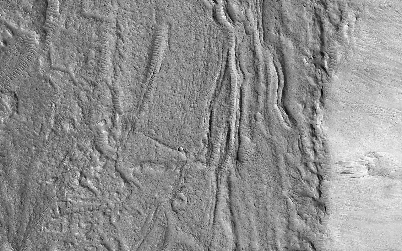 The geologic setting and latitude here suggest this is a glacial (ice-rich) flow, but the surface is broken into plates like many lava flows on Mars. An image was targeted here to get a better look.  At the meter-scale resolution of HiRISE, we see a hummocky surface with boulders and craters plus some wind-blown landforms that seems consistent with either the glacial or lava hypothesis. This is a common result: getting a higher-resolution image doesn't necessarily provide more information about large-scale processes, instead providing information about how the surface has been modified.  https://photojournal.jpl.nasa.gov/catalog/PIA25794