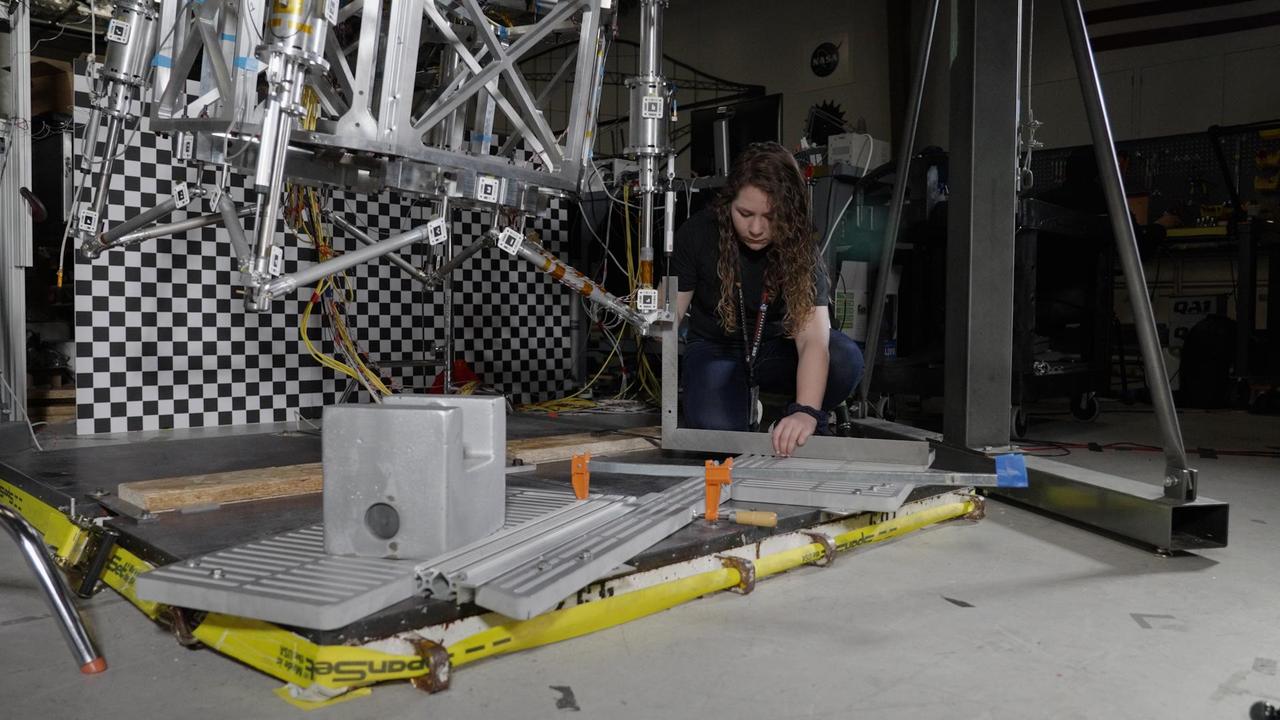Morgan Montalvo, an engineer at NASA's Jet Propulsion Laboratory, sets guardrails on the floor below a prototype of the lander being designed for the agency's Mars Sample Return campaign. These guardrails were used to test a scenario where the lander would "stub a toe" against a rock while touching down on Mars.  The Sample Retrieval Lander, estimated to weigh as much as 5,016 pounds (2,275 kilograms), would be the heaviest spacecraft ever to land on the Red Planet. To study the physics involved in landing such a massive spacecraft, engineers have been testing a lander prototype that's about one-third the size it would be on Mars.  Mars Sample Return will revolutionize our understanding of Mars by bringing scientifically selected samples to Earth for study using the most sophisticated instrumentation around the world. NASA's planned Mars Sample Return (MSR) campaign would fulfill one of the highest priority solar system exploration goals identified by the National Academies of Sciences, Engineering and Medicine in the past three decadal surveys. This strategic partnership with the ESA (European Space Agency) features the first mission to return samples from another planet, including the first launch from the surface of another planet. The samples being collected by NASA's Perseverance rover during its exploration of an ancient river delta are thought to be the best opportunity to reveal the early evolution of Mars, including the potential for ancient life.  https://photojournal.jpl.nasa.gov/catalog/PIA25823