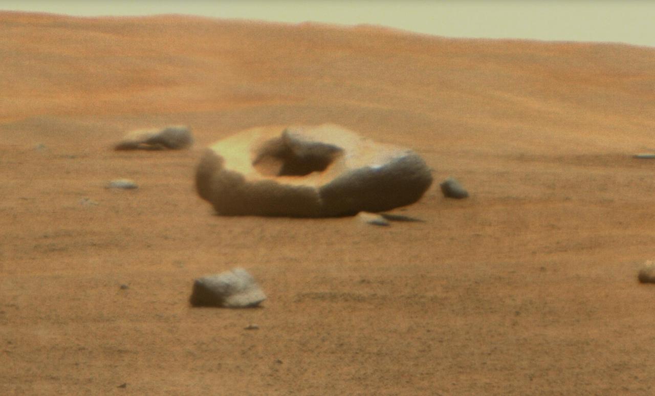 NASA's Perseverance Mars rover captured this doughnut-shaped rock in Jezero Crater from about 328 feet (100 meters) away using its Remote Microscopic Imager (RMI), part of the SuperCam instrument, on June 22, 2023, the 832nd Martian day, or sol, of the mission. Oddly shaped rocks aren't uncommon, either on Earth or Mars; they're often formed over eons as winds sandblast rock faces. This particular rock may have formed after a smaller rock (or multiple rocks) eroded near its center. That left behind a cavity that was later enlarged by the wind.  Figure A shows the same rock in its broader context, when it was first spotted by the rover's Mastcam-Z instrument from about 1,312 feet (400 meters away) on April 15, 2023, the 765th Martian day, or sol, of the mission.  SuperCam is led by Los Alamos National Laboratory in New Mexico, where the instrument's body unit was developed. That part of the instrument includes several spectrometers as well as control electronics and software. The mast unit, including RMI, was developed and built by several laboratories of the CNRS (the French research center) and French universities under the contracting authority of Centre National d'Études Spatiales (CNES), the French space agency.  Arizona State University leads the operations of the Mastcam-Z instrument, working in collaboration with Malin Space Science Systems in San Diego, on the design, fabrication, testing, and operation of the cameras, and in collaboration with the Niels Bohr Institute of the University of Copenhagen on the design, fabrication, and testing of the calibration targets.  A key objective for Perseverance's mission on Mars is astrobiology, including the search for signs of ancient microbial life. The rover will characterize the planet's geology and past climate, pave the way for human exploration of the Red Planet, and be the first mission to collect and cache Martian rock and regolith (broken rock and dust).  Subsequent NASA missions, in cooperation with ESA (European Space Agency), would send spacecraft to Mars to collect these sealed samples from the surface and return them to Earth for in-depth analysis.  The Mars 2020 Perseverance mission is part of NASA's Moon to Mars exploration approach, which includes Artemis missions to the Moon that will help prepare for human exploration of the Red Planet.  https://photojournal.jpl.nasa.gov/catalog/PIA25916