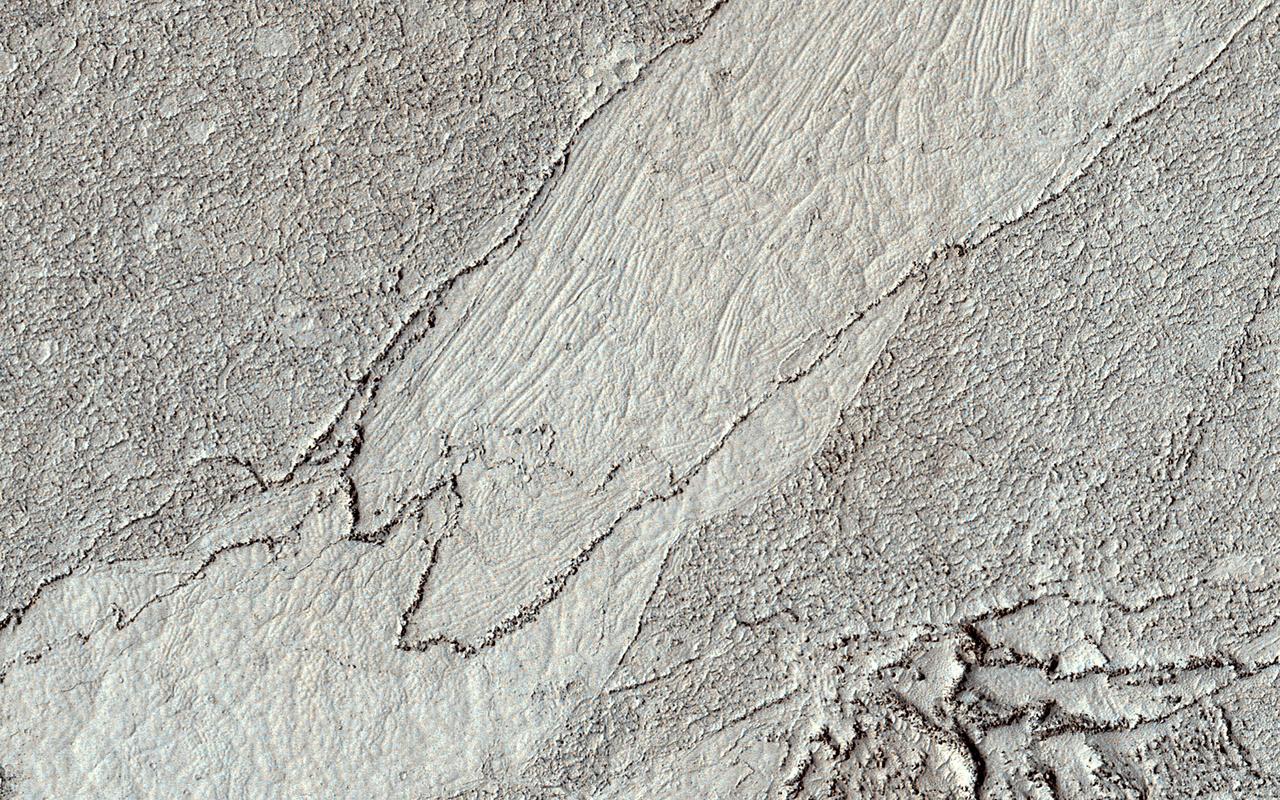 This HiRISE image shows a classic example of platy-ridged lava. Scientists think that this is the same as a lava type called "rubbly pahoehoe" on Earth.  In this lava, a crust of rubble forms as the lava partially cools but then tears up its own cover. Eventually, the rubble can form plates that can be rafted apart as the lava cools further, producing textures like those visible on terrestrial lava lakes that have cooled.  We see here a complex history of these processes. There are two different shapes of the rubble (at right, and top left/bottom center) indicating two stages of formation. The smooth area at center also is divided into two domains with different polygon styles, indicating that the rift opened, partially cooled, and then opened further.  https://photojournal.jpl.nasa.gov/catalog/PIA25948