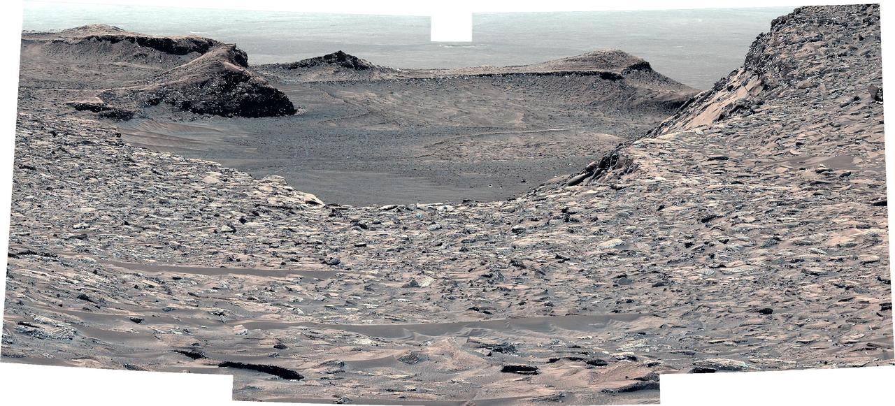 NASA's Curiosity Mars rover looks back down at "Marker Band Valley" after climbing a steep slope. This mosaic, made of five images that were stitched together after being sent to Earth, was captured by the rover's Mastcam on June 21, 2023, the 3,865th Martian day, or sol, of the mission. The color has been adjusted to match lighting conditions as the human eye would see them on Earth. Curiosity struggled to climb a 23-degree slope that had slippery sand and wheel-size boulders. These three factors – the incline, the sand, and the large boulders – combined to make this Curiosity's toughest climb yet. https://photojournal.jpl.nasa.gov/catalog/PIA26011