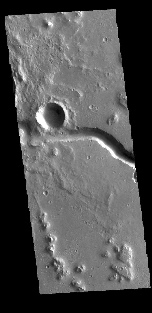 This VIS image shows part of Hephaestus Fossae. Hephaestus Fossae is a complex channel system in Utopia Planitia near Elysium Mons. It has been proposed that the channel formed by the release of melted subsurface ice during the impact event that created the crater just off the left side of the image – only the ejecta is seen in this image. The crater is fairly young, as there is only minimal modification of the crater floor. While it appears that the crater sits of top of the channel, the creation of the crater may have also created the channel. The impact event would have caused subsurface heating, melting any subsurface ice in the region which would have created surface flow to form the channel. Additionally, the nearby Elysium volcanic center created subsurface heating that may have played a part in creating both Hephaestus Fossae and Hebrus Valles to the north. Orbit Number: 94645 Latitude: 17.6141 Longitude: 126.055 Instrument: VIS Captured: 2023-04-16 09:02 https://photojournal.jpl.nasa.gov/catalog/PIA26040