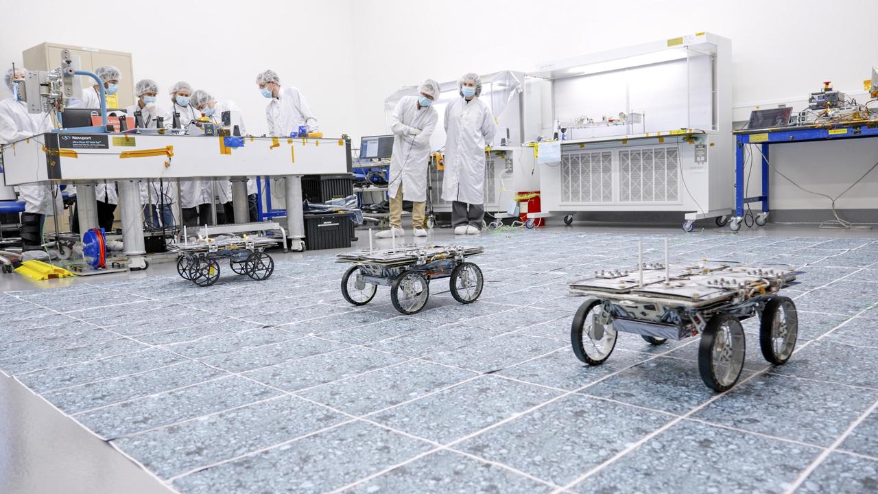 Engineers prepare three small Moon-bound rovers for a drive test in a clean room at the agency's Jet Propulsion Laboratory in Southern California in December 2023. Along with a base station that will be mounted on a lunar lander, the rovers make up the CADRE (Cooperative Autonomous Distributed Robotic Exploration) technology demonstration.  This image was taken during a test of the rovers' ability to drive together as a team autonomously, without explicit commands from engineers. If the project succeeds, future missions could include teams of robots spreading out to take simultaneous, distributed scientific measurements, potentially in support of astronauts.  In this test, the rovers had their solar panels closed, and they wore protective black plastic covers over their ultralight aluminum wheels to prevent the wheels' grousers from catching on the clean room floor.  https://photojournal.jpl.nasa.gov/catalog/PIA26164