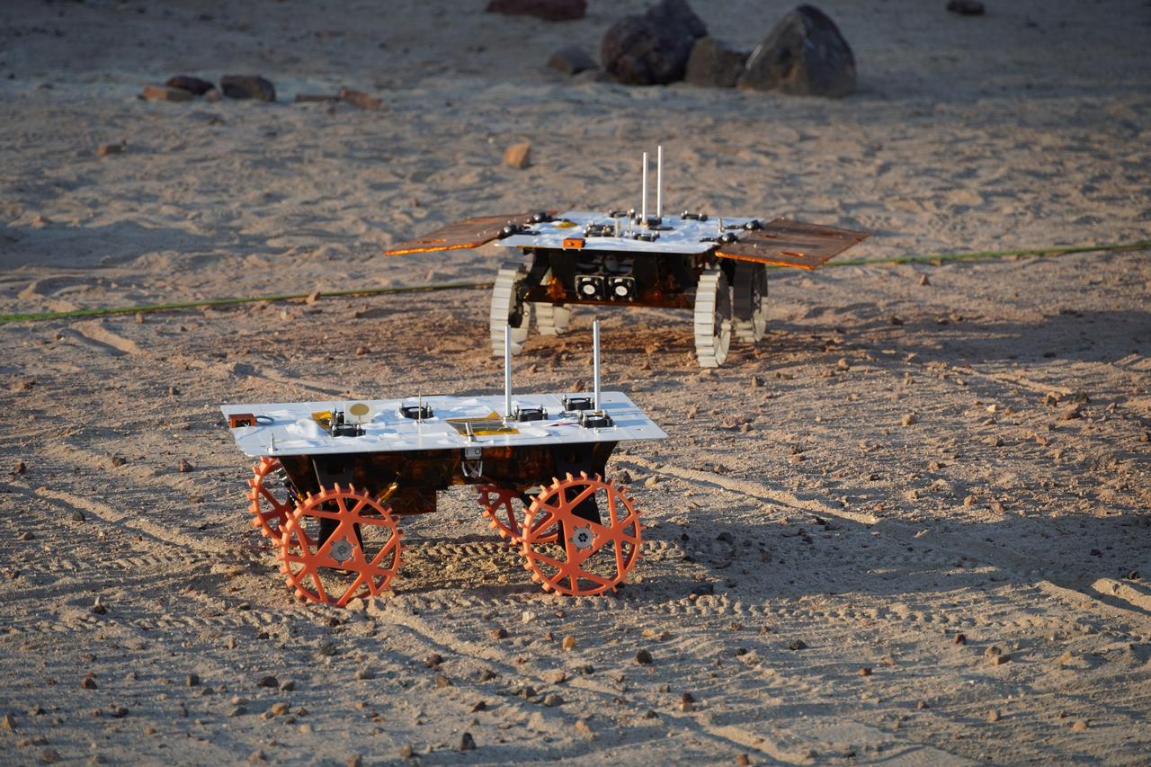 Two full-scale development model rovers that are part of NASA's CADRE (Cooperative Autonomous Distributed Robotic Exploration) technology demonstration drive in the Mars Yard at the agency's Jet Propulsion Laboratory in Southern California in August 2023. The project is designed to show that a group of robotic spacecraft can work together as a team to accomplish tasks and record data autonomously – without explicit commands from mission controllers on Earth. The rovers being tested here are similar in size and appearance to the flight models – still being built at the time of this image – that will travel to the Moon. Equipped with flight software and autonomy capabilities, these development models were used for drive tests outside the clean room. In this image, one rover is fitted with a stand-in for solar panels, while the other rover is not. A series of Mars Yard tests with the development models confirmed CADRE hardware and software can work together to accomplish key goals for the project. The rovers drove together in formation. Faced with unexpected obstacles in the way, they adjusted their plans as a group by sharing updated maps and replanning coordinated paths. And when one rover was low on battery charge, the whole team paused so they could later continue together. Several drives were performed at night under large flood lamps so the rovers could experience extreme shadows and lighting that approximate what they'll encounter during the lunar daytime. https://photojournal.jpl.nasa.gov/catalog/PIA26168