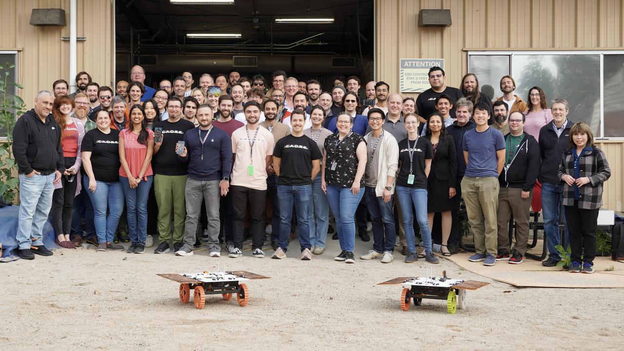 Members of NASA's CADRE (Cooperative Autonomous Distributed Robotic Exploration) technology demonstration team pose with two full-scale development model rovers in the Mars Yard at the agency's Jet Propulsion Laboratory in Southern California in January 2024. The project is designed to show that a group of robotic spacecraft can work together as a team to accomplish tasks and record data autonomously – without explicit commands from mission controllers on Earth. Three small rovers will ride aboard a lunar lander that will carry the project's base station and camera assembly. The rovers shown here are similar in size and appearance to the flight models that will travel to the Moon. Equipped with flight software and autonomy capabilities, these development models were used in a series of Mars Yard tests that helped confirm CADRE hardware and software can work together to accomplish key goals for the project. https://photojournal.jpl.nasa.gov/catalog/PIA26170