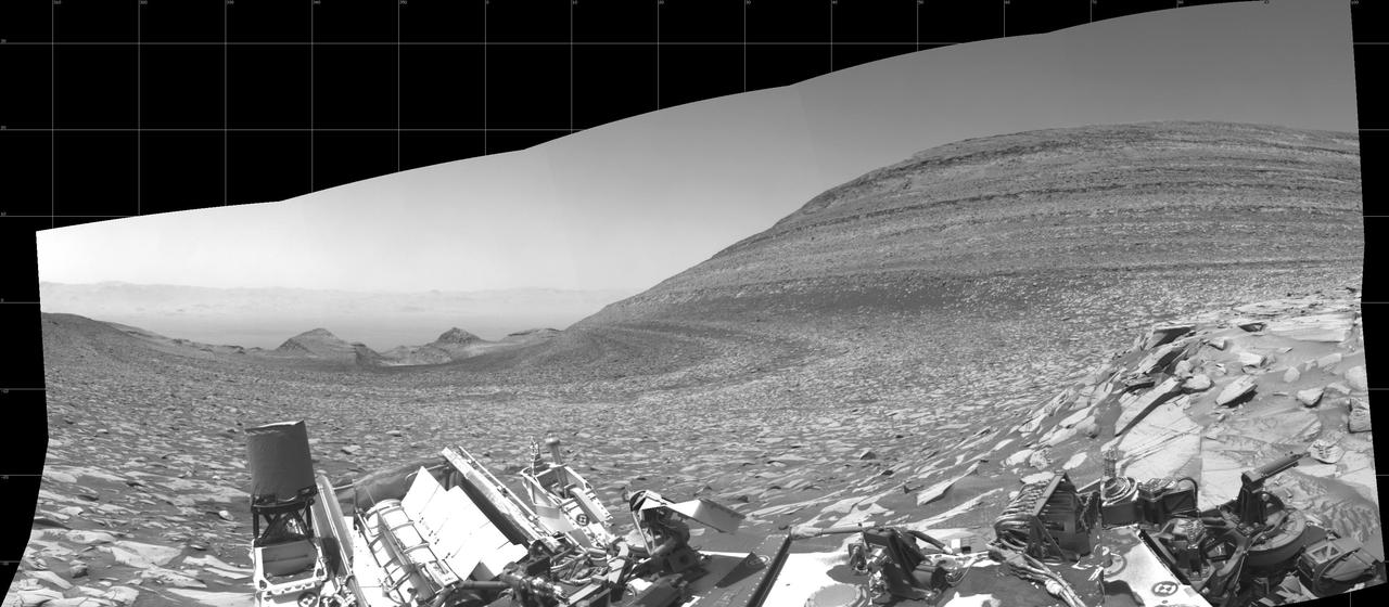 NASA's Curiosity Mars rover captured this panorama – showing the area it climbed to reach Gediz Vallis channel – using its left black-and-white navigation camera on Feb. 1, 2024, the 4,084th Martian day, or sol, of the mission. The panorama is made up of 10 images that were stitched together after being sent back to Earth. At center is the slope Curiosity ascended, which is striped with alternating dark and light bands of sedimentary rock. Farther down the slope are two buttes: "Chenapau" on the left and "Orinoco" on the right. Farther still is the floor of Gale Crater, with the crater's rim in the far distance. At right rises a banded butte nicknamed "Kukenán." Since 2014, Curiosity has been ascending the foothills of Mount Sharp, which stands 3 miles (5 kilometers) above the floor of Gale Crater. The layers in this lower part of the mountain formed over millions of years under a changing Martian climate, providing scientists with a way to study how the presence of both water and the chemical ingredients required for life changed over time. https://photojournal.jpl.nasa.gov/catalog/PIA26247
