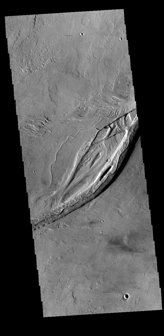 Olympica Fossae is a complex channel located on the volcanic plains between Alba Mons and Olympus Mons. It contains both linear sections that appear to be tectonic in origin and sinuous sections that were more likely created by liquid flow. There are several streamlined islands in this image, indicating a fluvial origin in this section of the fossae. Given the location it appears that lava, rather than water, was the fluid. Olympica Fossae 420km long (261 miles). Orbit Number: 95165 Latitude: 23.3032 Longitude: 243.696 Instrument: VIS Captured: 2023-05-29 04:39 https://photojournal.jpl.nasa.gov/catalog/PIA26264
