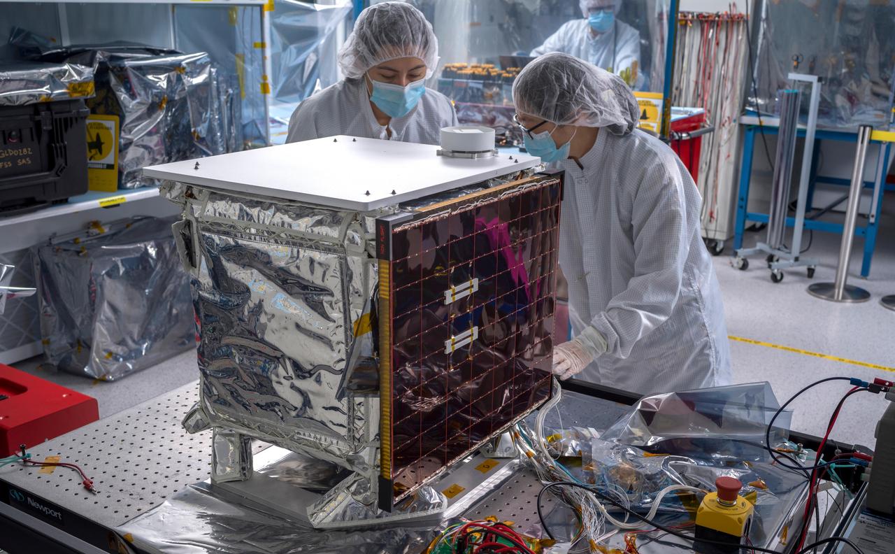 In a clean room at NASA's Jet Propulsion Laboratory in Southern California in March 2024, engineers and technicians work to prepare the agency's Farside Seismic Suite (FSS) for environmental testing to simulate conditions it will encounter in space. Along with being placed in a vacuum chamber and subjected to extreme temperatures, the instrument suite will undergo severe shaking that mimics the rocket's motion during launch.  The cube-shaped payload contains two instruments that will gather NASA's first seismic data from the Moon in nearly 50 years and take the first-ever seismic measurements from the Moon's far side. FSS will operate continuously for at least 4½ months, working through the long, cold lunar nights.  The two seismometers are packaged together with a large battery, a computer, and electronics inside a cube structure that's surrounded by several layers of insulation and suspended within an outer protective cube, which is in turn covered with a shiny insulating blanket. The suite's single solar panel can be seen at center. On top is a white radiator that will allow the suite to shed heat generated by its electronics during the hot lunar daytime hours. The puck-like object atop the radiator is the suite's antenna, for communicating with two small relay satellites that will orbit the Moon and send data to Earth.  Pictured (from left): Joanna Farias, and Bert Turney, and Hsin-Yi Hao.  https://photojournal.jpl.nasa.gov/catalog/PIA26299