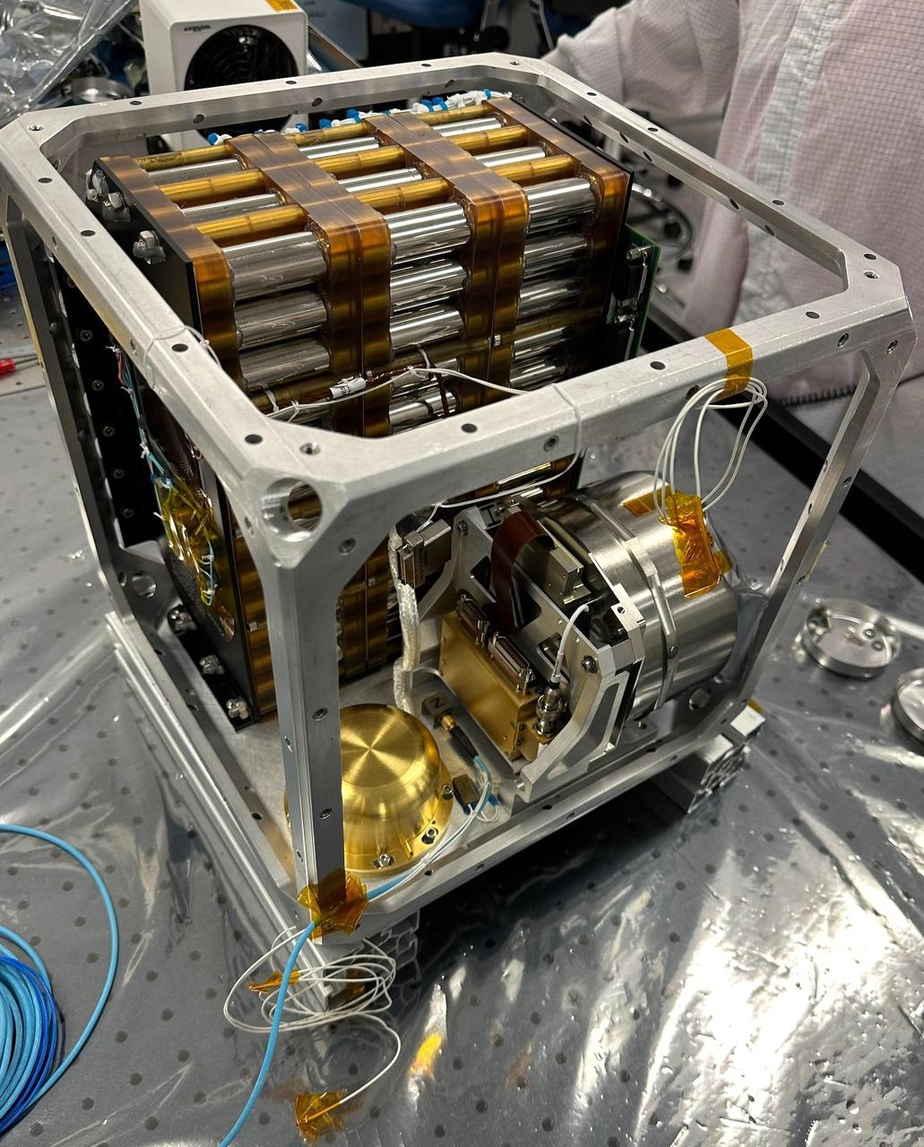 NASA's Farside Seismic Suite (FSS) is assembled in a clean room at the agency's Jet Propulsion Laboratory in Southern California in November 2023. Two sensitive seismometers packaged in the suite's cube-within-a-cube structure will gather NASA's first seismic data from the Moon in nearly 50 years and take the first-ever seismic measurements from the Moon's far side. FSS will operate continuously for at least 4½ months, working through the long, cold lunar nights.  Seen here is the inner cube structure, with the suite's large battery at rear. The gold, puck-shaped device at left is the Short Period sensor, or SP, which measures motion in three directions using sensors etched into a trio of square silicon chips, each about 1 inch (25 millimeters) wide. At right, within the silver cylindrical enclosure, is the Very Broadband seismometer, or VBB, the most sensitive seismometer ever built for use in space exploration. It can detect ground motions smaller than the size of a single hydrogen atom, measuring up-and-down movement using a pendulum held in place by a spring. Constructed as a backup instrument (a "flight spare") for NASA's InSight Mars lander by the French space agency, CNES (Centre National d'Études Spatiales), the VBB was slightly modified and packaged in a new enclosure for lunar use. The suite's computer and electronics are packed alongside the battery and seismometers.  After being encased in insulation, this inner cube was suspended within a protective outer cube, which was in turn covered with a shiny insulating blanket.  https://photojournal.jpl.nasa.gov/catalog/PIA26300