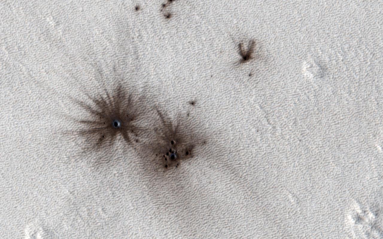 HiRISE and the Context Camera (CTX, also on board the Mars Reconnaissance Orbiter) are always on the lookout for new impact craters. New impacts can be identified by comparing images of the same region taken at different times (typically years apart) and looking for visual clues of recent impacts.  CTX is more adept at identifying new impacts because of its larger and repeated surface coverage, but HiRISE allows us to study those impacts in higher resolution. In this image, we can see multiple dark spots corresponding to numerous new craters. We can also identify a slightly larger crater, and a number of smaller ones, particularly in a cluster next to it. That clustering gives us the first indication that these craters were formed in a single event.  As the impactor was falling towards Mars, the friction with the atmosphere led to the body fragmenting into smaller pieces shortly before striking the surface creating this notable pattern.  https://photojournal.jpl.nasa.gov/catalog/PIA26322