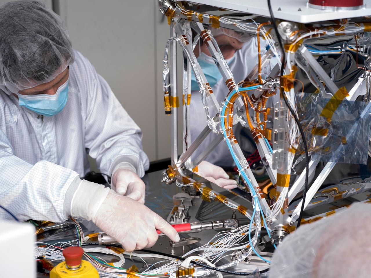 In a clean room at NASA's Jet Propulsion Laboratory in Southern California in March 2024, technician Nik Schwarz prepares the agency's Farside Seismic Suite (FSS) for testing. The cube-shaped payload contains two instruments that will gather NASA's first seismic data from the Moon in nearly 50 years and take the first-ever seismic measurements from the Moon's far side. FSS will operate continuously for at least 4½ months, working through the long, cold lunar nights.  The two seismometers are packaged together with a large battery, a computer, and electronics inside a cube structure that's surrounded by several layers of insulation (the shiny, reflective material seen here) and suspended within an outer protective cube, which is in turn covered with a shiny insulating blanket. A technician is here attaching a stiffening brace to the bottom of the FSS outer cube structure.  https://photojournal.jpl.nasa.gov/catalog/PIA26341