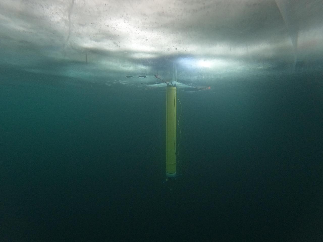       A prototype of an autonomous robot, part of a project called IceNode being developed at NASA's Jet Propulsion Laboratory, is seen from beneath the frozen surface of Lake Superior, off Michigan's Upper Peninsula. The three thin legs of the robot's "landing gear" affix it to the icy ceiling. A remote camera captured the image during a field test in 2022.      The IceNode project envisions a fleet of such robots to venture beneath Antarctic ice shelves and gather data that would help scientists calculate how rapidly the ice shelves there are melting – and how fast that melting could cause global sea levels to rise.      Each about 8 feet (2.4 meters) long and 10 inches (25 centimeters) in diameter, the robots use three-legged "landing gear" that springs out from one end to attach the robot to the underside of the ice. Rather than using propulsion, the robots would autonomously position themselves with the help of novel algorithms based on models of ocean currents. Released from a borehole or a vessel in the open ocean, the robots would ride those currents on a long journey beneath an ice shelf.      They would target the underwater area known as the "grounding zone," where floating ice shelves, ocean, and land meet, deep inside unmapped cavities where the ice may be melting the fastest. Each robot would detach a ballast and rise up to affix itself to the underside of the ice, where their suite of sensors would measure how fast warm, salty ocean water is circulating up to melt the ice, and how quickly cold meltwater is sinking.      As conceived, the IceNode fleet would operate for up to a year, continuously capturing data, including seasonal fluctuations. Then the robots would detach themselves from the ice, drift back out to open ocean, and transmit their data via satellite.      This test was conducted through the U.S. Navy Arctic Submarine Laboratory's biennial Ice Camp, a three-week operation that provides researchers a temporary base camp from which to conduct field work in the harsh Arctic environment.      IceNode has been funded through JPL's internal research and technology development program and its Earth Science and Technology Directorate. JPL is managed for NASA by Caltech in Pasadena, California.  https://photojournal.jpl.nasa.gov/catalog/PIA26421