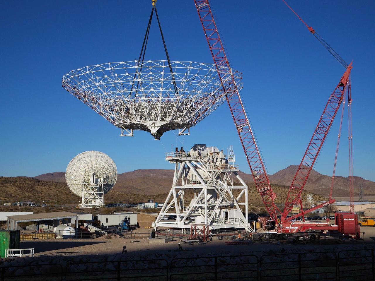 A crane lowers the 112-foot-wide (34-meter-wide) steel framework for the Deep Space Station 23 (DSS-23) reflector dish into position on Dec. 18, 2024, at the Deep Space Network's Goldstone Space Communications Complex near Barstow, California. A multi-frequency beam waveguide antenna, DSS-23 will boost the DSN's capacity and enhance NASA's deep space communications capabilities for decades to come.  Once online in 2026, DSS-23 will be the fifth of six new beam waveguide antennas to be added to the network, following DSS-53, which was added at the DSN's Madrid complex in 2022.  After the reflector skeleton was bolted into place, engineers placed what's called a quadripod into the center of the structure. A four-legged support structure weighing 16 ½ tons, the quadripod is fitted with a curved subreflector that will direct radio frequency signals from deep space that bounce off the main reflector into the antenna's pedestal where the antenna's receivers are housed.  Next steps: to fit panels onto the steel skeleton of the parabolic reflector to create a curved surface to collect radio frequency signals.  The DSN allows missions to track, send commands to, and receive scientific data from faraway spacecraft. It is managed by NASA's Jet Propulsion Laboratory in Southern California for the agency's Space Communications and Navigation (SCaN) program, which is located at NASA Headquarters within the Space Operations Mission Directorate.  https://photojournal.jpl.nasa.gov/catalog/PIA26454