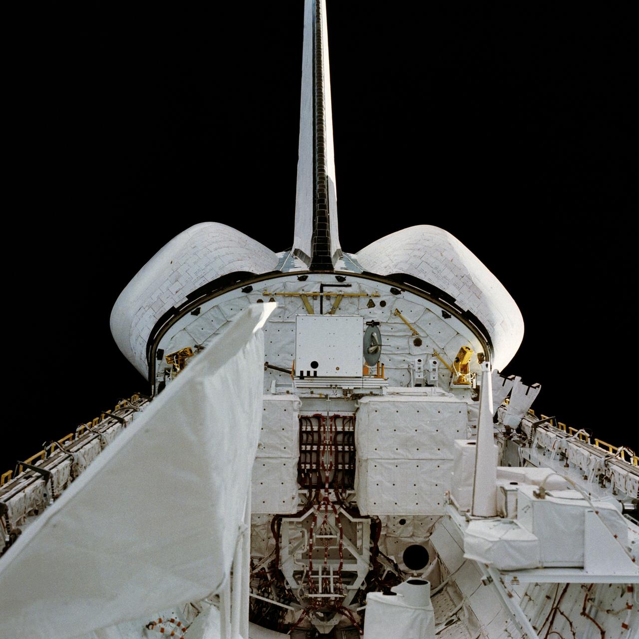 STS002-13-208 (12-14 Nov. 1981) --- This clear view of the aft section of the Earth-orbiting space shuttle Columbia's cargo bay and some of its cargo was photographed through the flight deck's aft windows. Visible in the center of the photo are the twin orbital maneuvering system (OMS) pods. The vertical stabilizer or tail splits the top part of the image in half. The Induced Environment Contamination Monitor (IECM) Location experiment is located in the back center of the cargo bay, near the top. There is a grapple fixture attached to the side of the IECM. Various components of the Office of Space Terrestrial Applications (OSTA-1) payload are seen near the aft section of the cargo bay, such as the Feature Identification and Location Experiment (FILE) (the long cone shaped object on the right back), the Shuttle Multispectral Infrared Radiometer (SMIRR) (on pallet base) and the SIR-A recorder in the right foreground. In the left foreground the Shuttle Imaging Radar-A (SIR-A) antenna can be seen. Photo credit: NASA