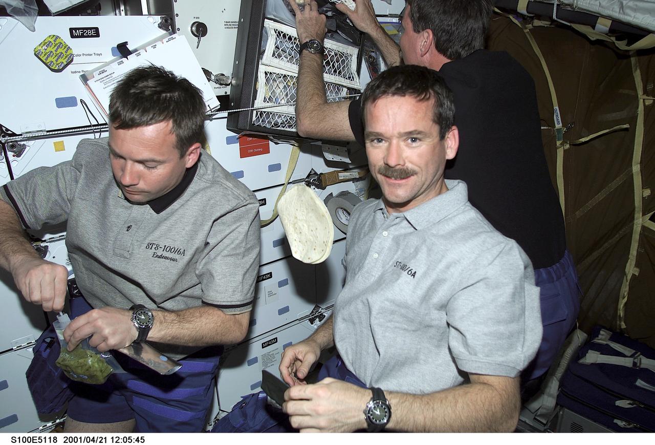 S100-E-5118 (21 April 2001) --- Astronaut Chris A. Hadfield (center) of the Canadian Space Agency and cosmonaut Yuri V. Lonchakov (left) of Rosaviakosmos, are about to be joined by astronaut Scott E. Parazynski (background) as the three STS-100 mission specialists take time on the middeck of the Space Shuttle Endeavour for a meal. The seven-member STS-100 crew has been busy preparing for its union with the International Space Station (ISS). The image was recorded with a digital still camera.