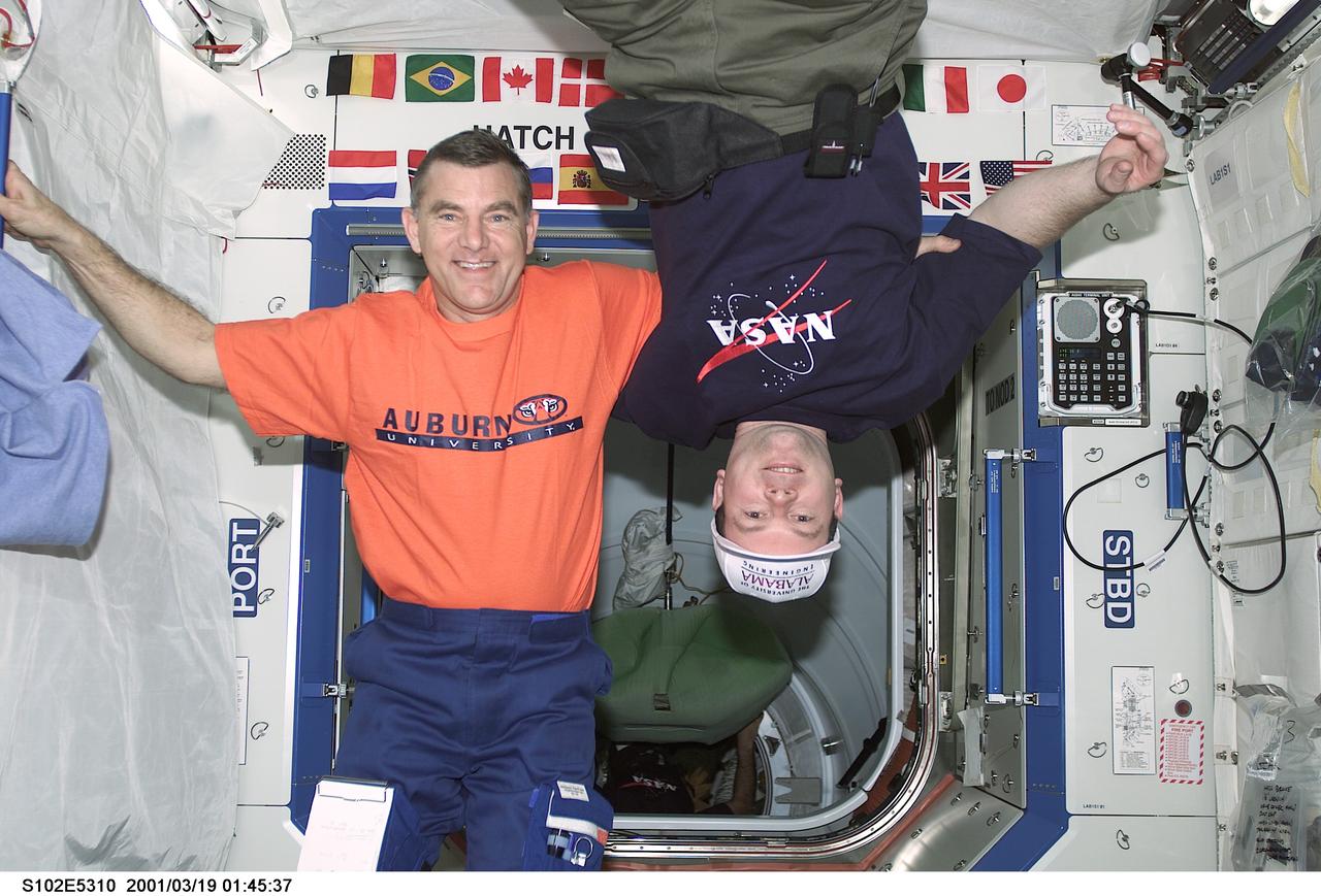STS102-E-5310 (19 March 2001) --- Astronauts James S. Voss (left) and James M. Kelly share a friendly moment onboard the International Space Station's U.S. laboratory Destiny in spite of the long-standing academic/athletic rivalry between their respective alma maters--Auburn University and the University of Alabama.  Voss, STS-102 mission specialist-turned Expedition Two flight engineer and a 1972 alumnus of Auburn with a bachelor of science degree in aerospace engineering, sports a T-shirt paying tribute to his university.  Kelly, STS-102 pilot and masters of science degree graduate in aerospace engineering from the University of Alabama in 1996, is wearing a cap from that institution of higher learning.