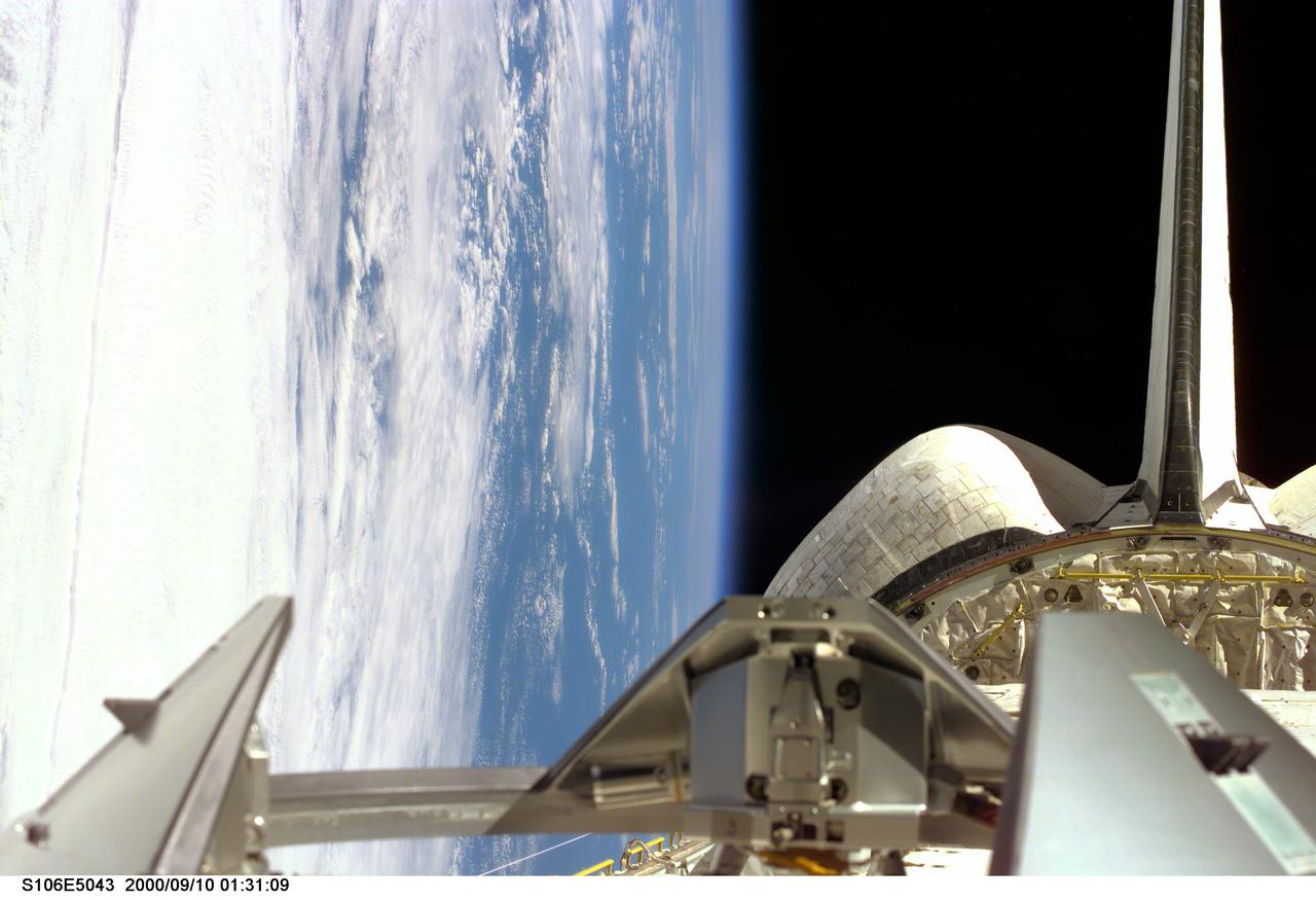 S106-E-5043 (10 September 2000) ---  An electronic still camera (ESC), aimed through the aft flight deck windows of the Space Shuttle Atlantis crew cabin ,  recorded this image of the cargo bay backdropped against clouds and water on Earth. The docking mechanism in the foreground awaits the upcoming rendezvous with the International Space Station (ISS) a little later in the 11-day mission.