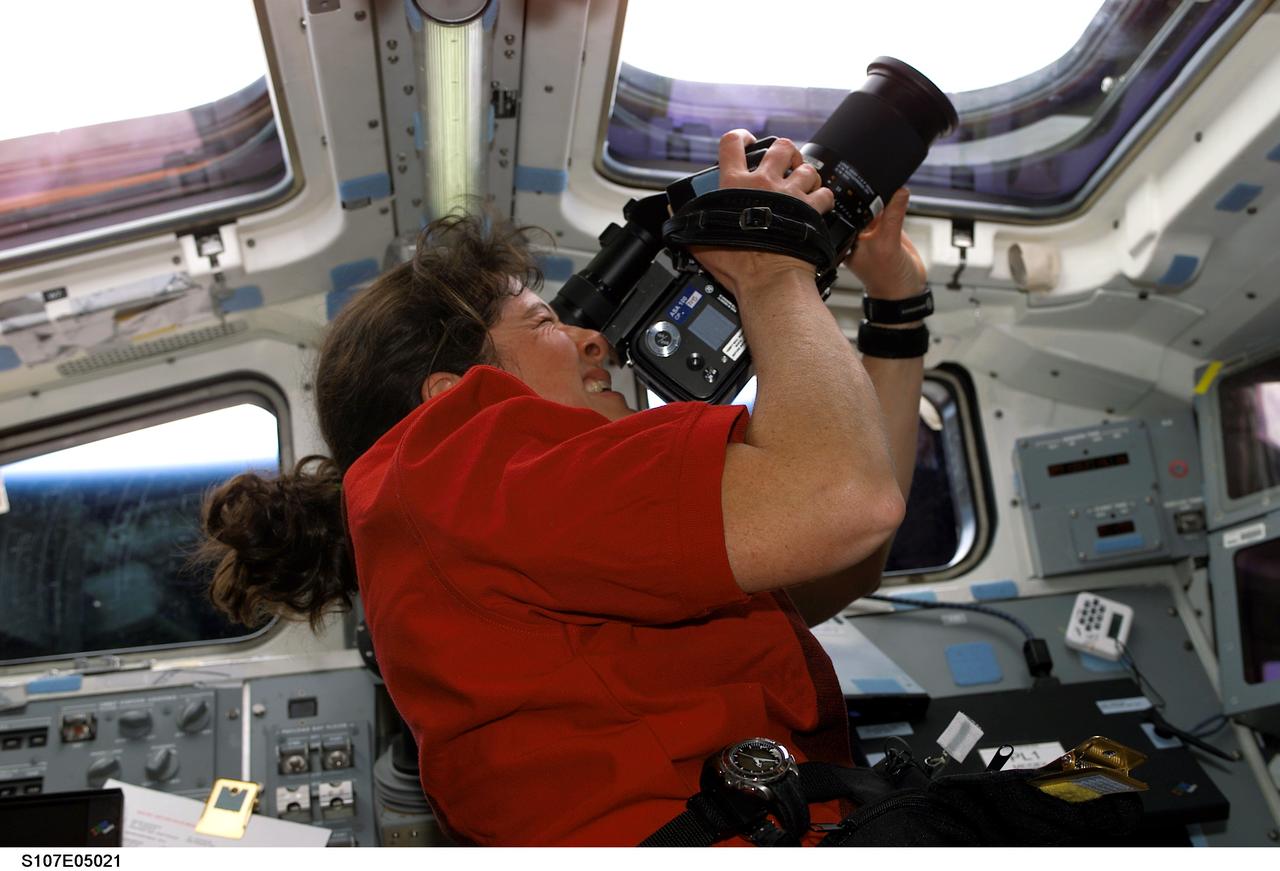 STS107-E-05021 (17 January 2003) --- Astronaut Laurel B. Clark, STS-107 mission specialist, uses a camera to photograph the topography of a point on Earth from an overhead window on the aft flight deck of the Earth-orbiting Space Shuttle Columbia.