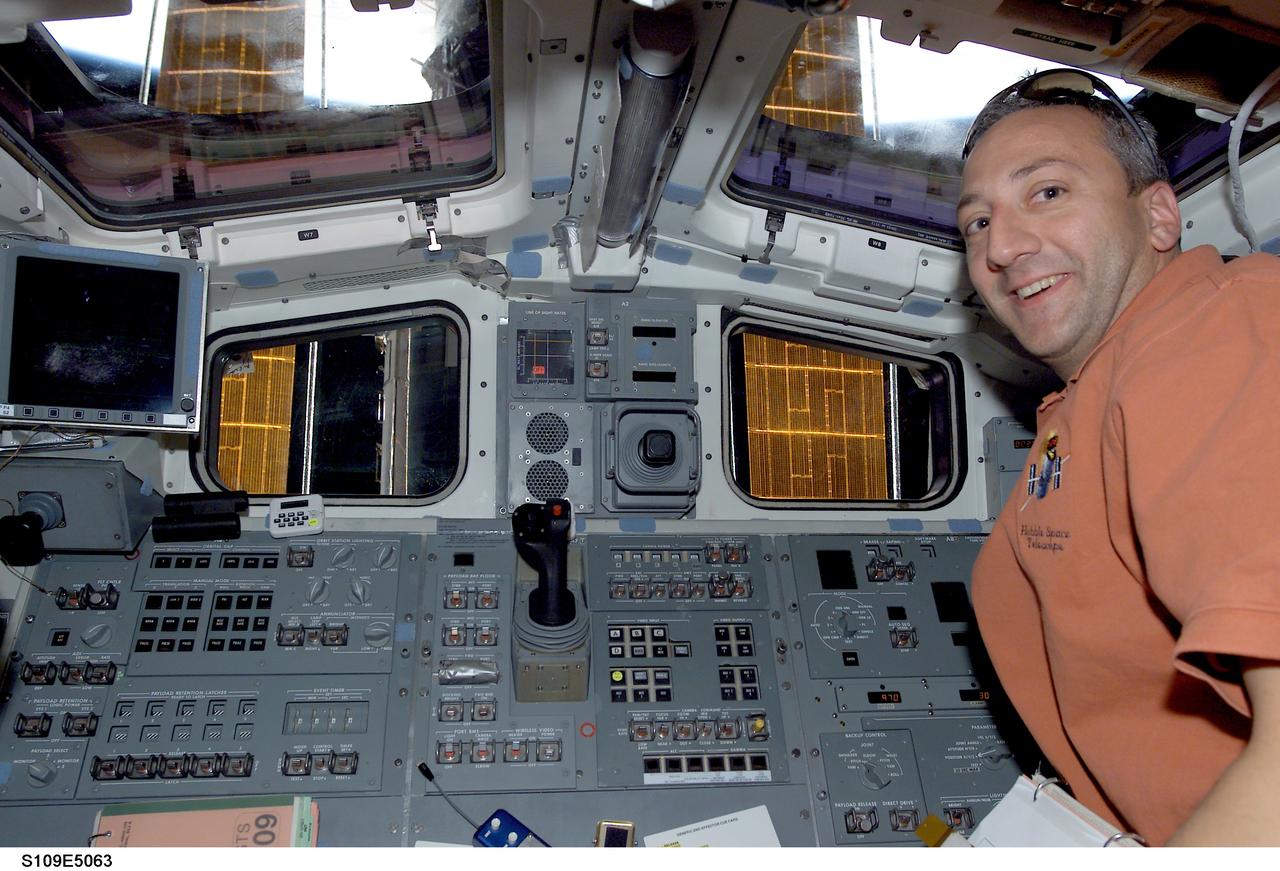 STS109-E-5063 (3 March 2002)  --- Astronaut Michael J. Massimino, STS-109 mission specialist, is pictured near the aft flight deck controls for the Space Shuttle Columbia shortly after the crew latched the Hubble Space Telescope (HST) into the shuttle's cargo bay. The telescope is partially visible through the cabin's rear windows. The image was taken with a digital still camera.