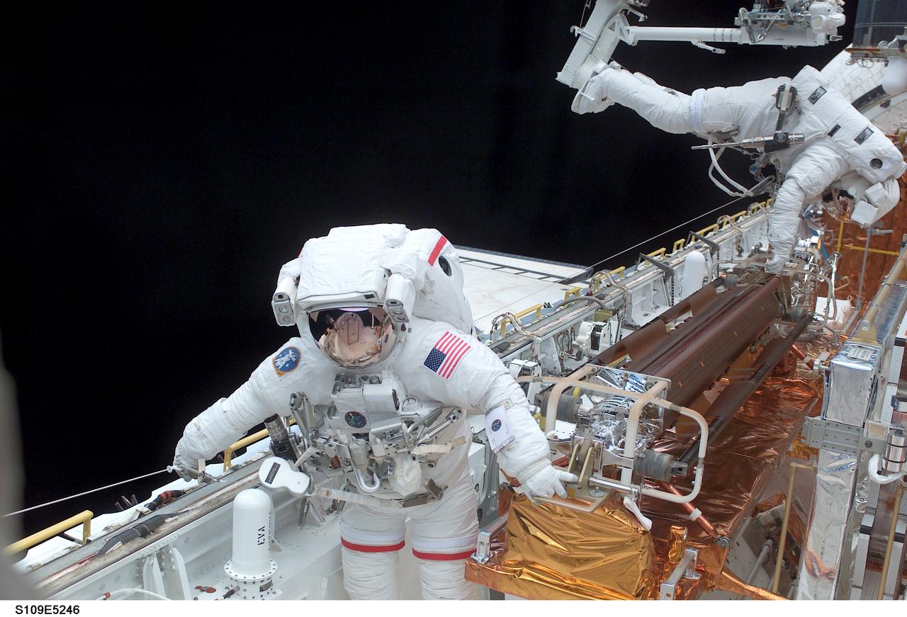 STS109-E-5246 (4 March 2002) ---  Astronaut John M. Grunsfeld (foreground), payload commander, is seen at one end of stowed solar panels in the cargo bay of the Space Shuttle Columbia while astronaut Richard M. Linnehan, mission specialist, uses the Remote Manipulator System's robotic arm to move around at the other end. The two, participating in the first of their assigned STS-109 space walks to perform work on the Hubble Space Telescope (HST), went on to replace the giant telescope&#0146;s starboard solar array. Their seven-hour space walk ended at 7:38 a.m. (CST) or 13:38 GMT March 4, 2002.